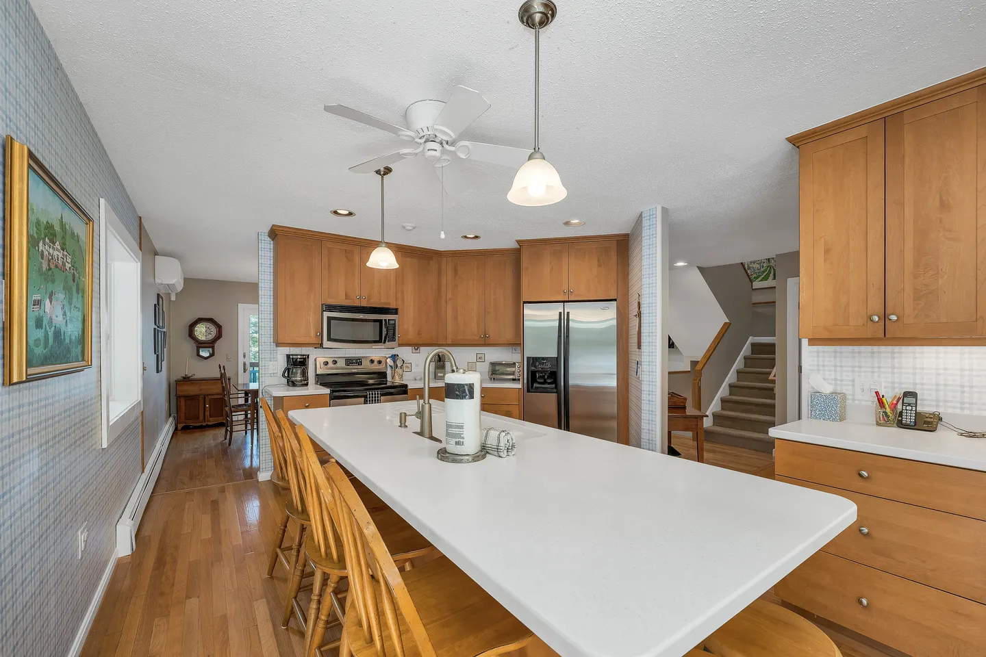 Kitchen with large center island, wooden barstools, light wood cabinets, and stainless steel appliances.
