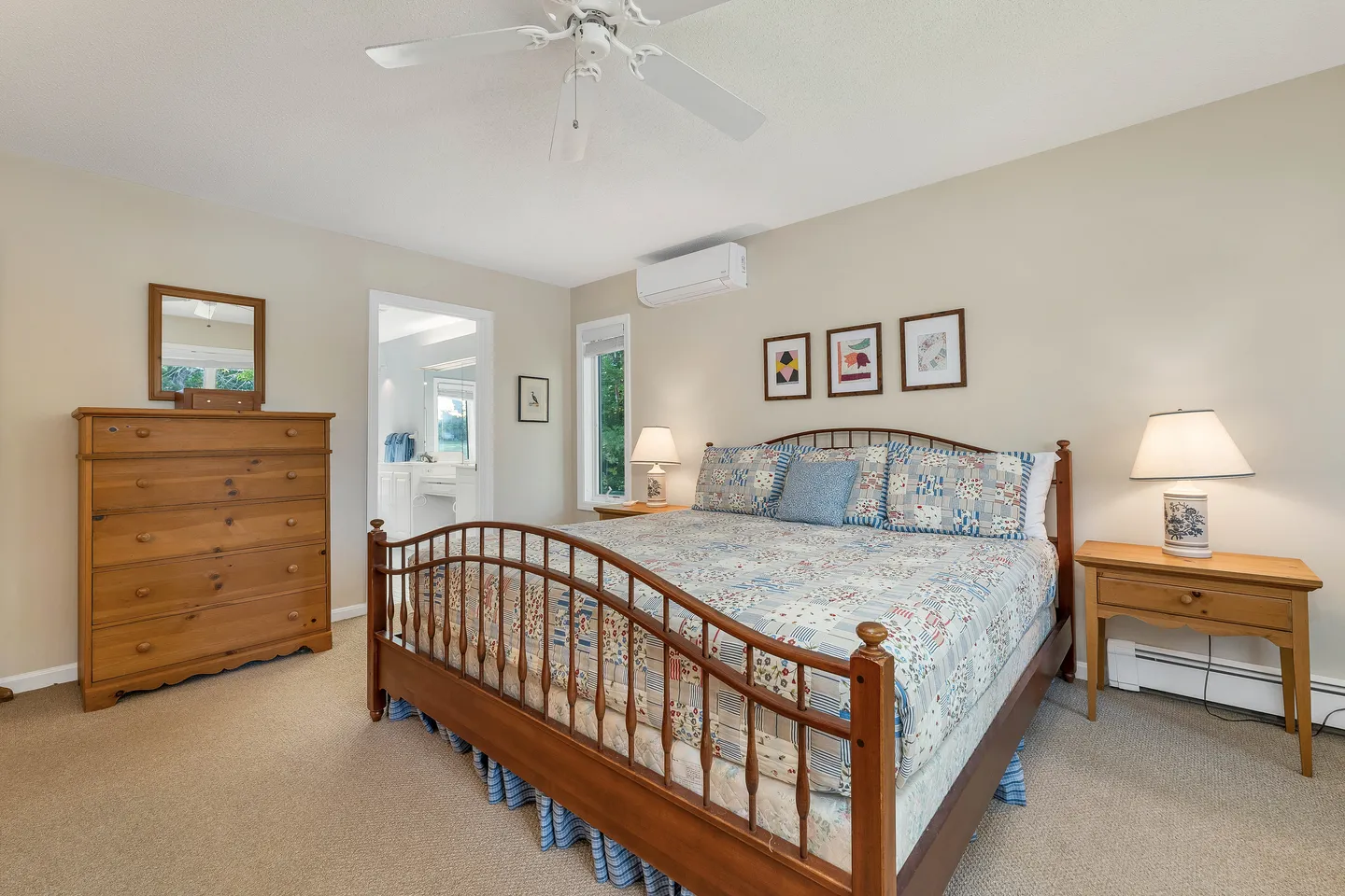 Bedroom featuring a wooden spindle bed with a patchwork quilt, wooden nightstands with lamps, a tall dresser, and an open doorway to an ensuite bathroom.