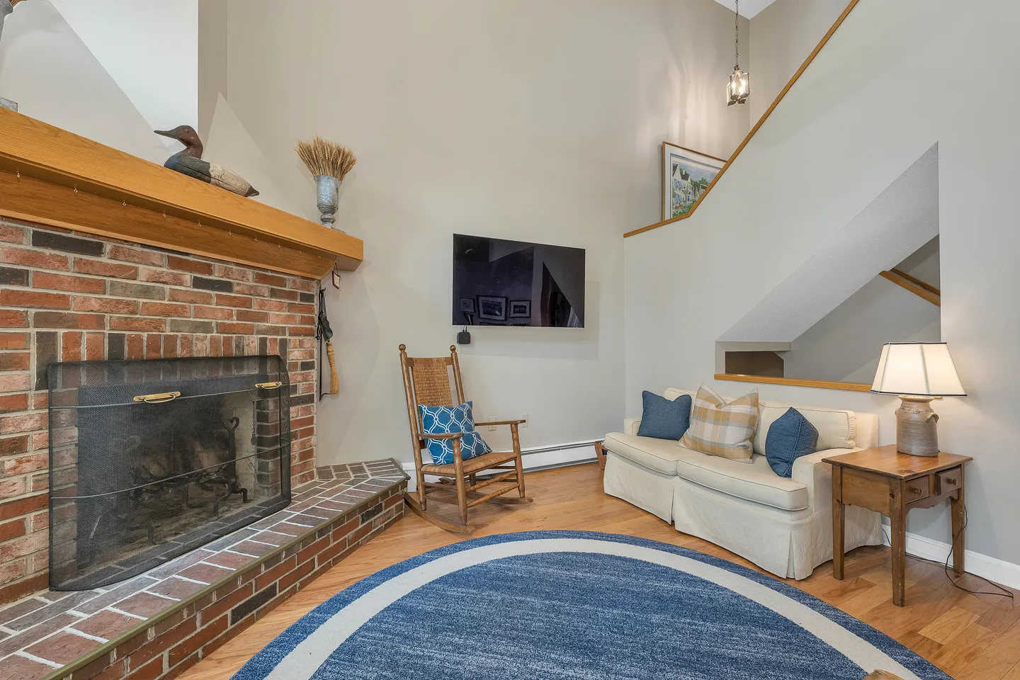 Living room featuring a brick fireplace with a wood mantel, a wall-mounted TV, a loveseat, and a rocking chair on wood flooring.