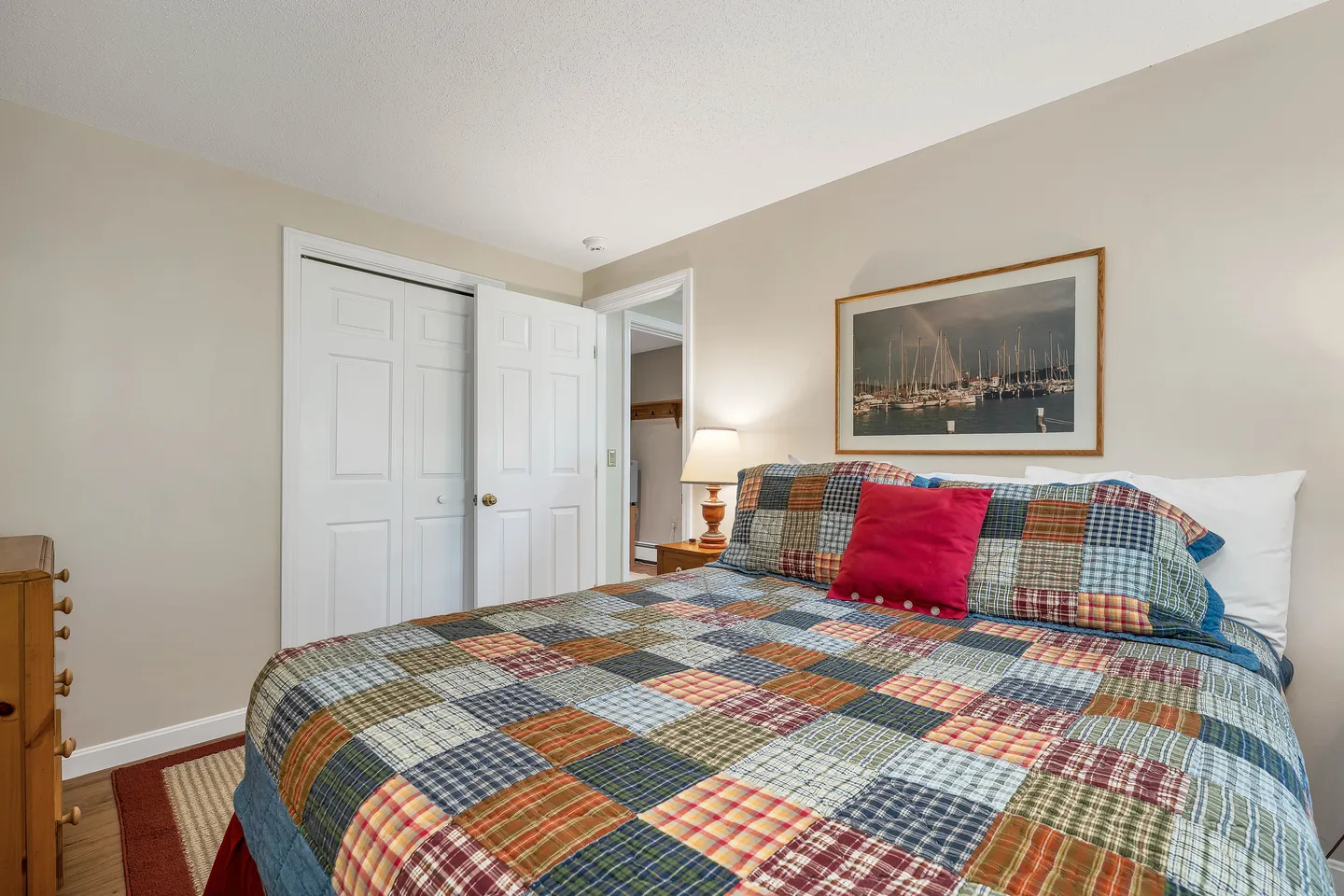Bedroom featuring a bed with a colorful patchwork quilt, a nightstand with a lamp, a framed picture on the wall, and a closet with white bifold doors.