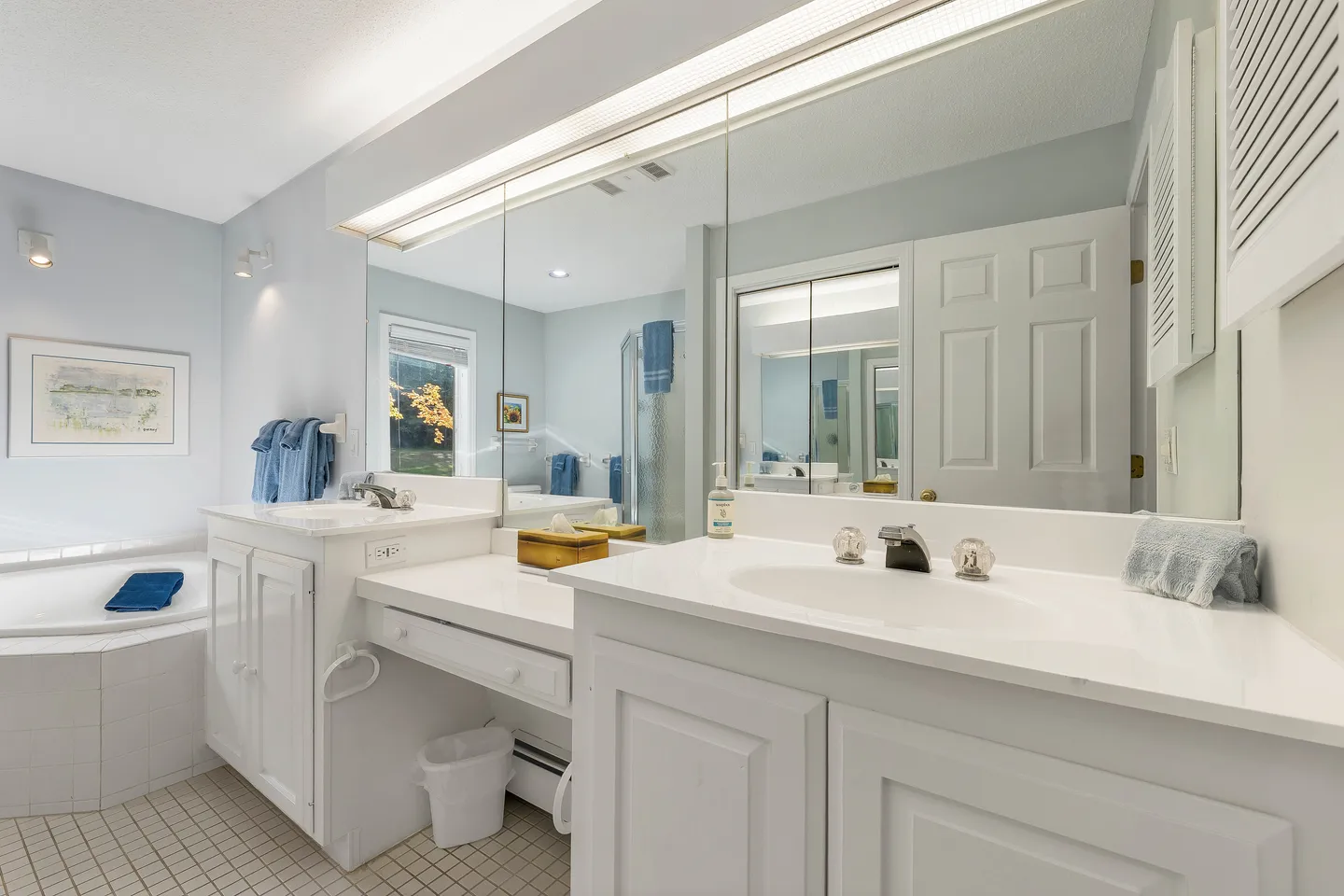 Bathroom with a double vanity, large mirror, tiled floor, and a corner bathtub.