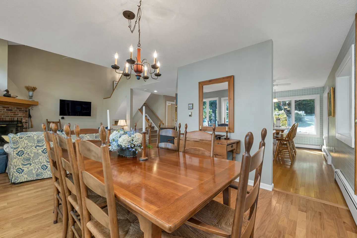 Dining room with a polished wood table, high-back wooden chairs, and a chandelier, looking toward a living room and hallway.