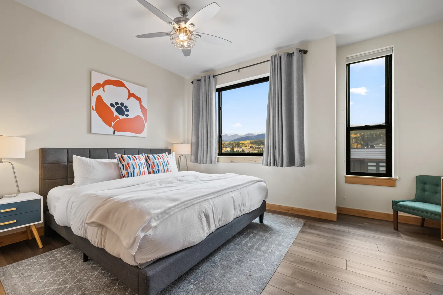 Bedroom with an upholstered bed, nightstand, ceiling fan, and large window overlooking mountain scenery.