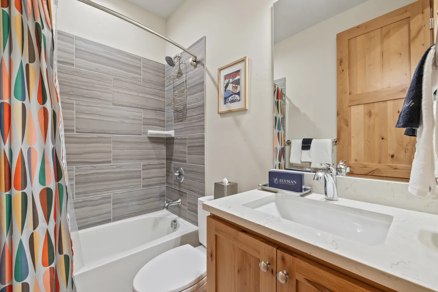 Bathroom with a bathtub and shower surrounded by horizontal gray tile, adjacent to a wooden vanity with a white countertop and sink.