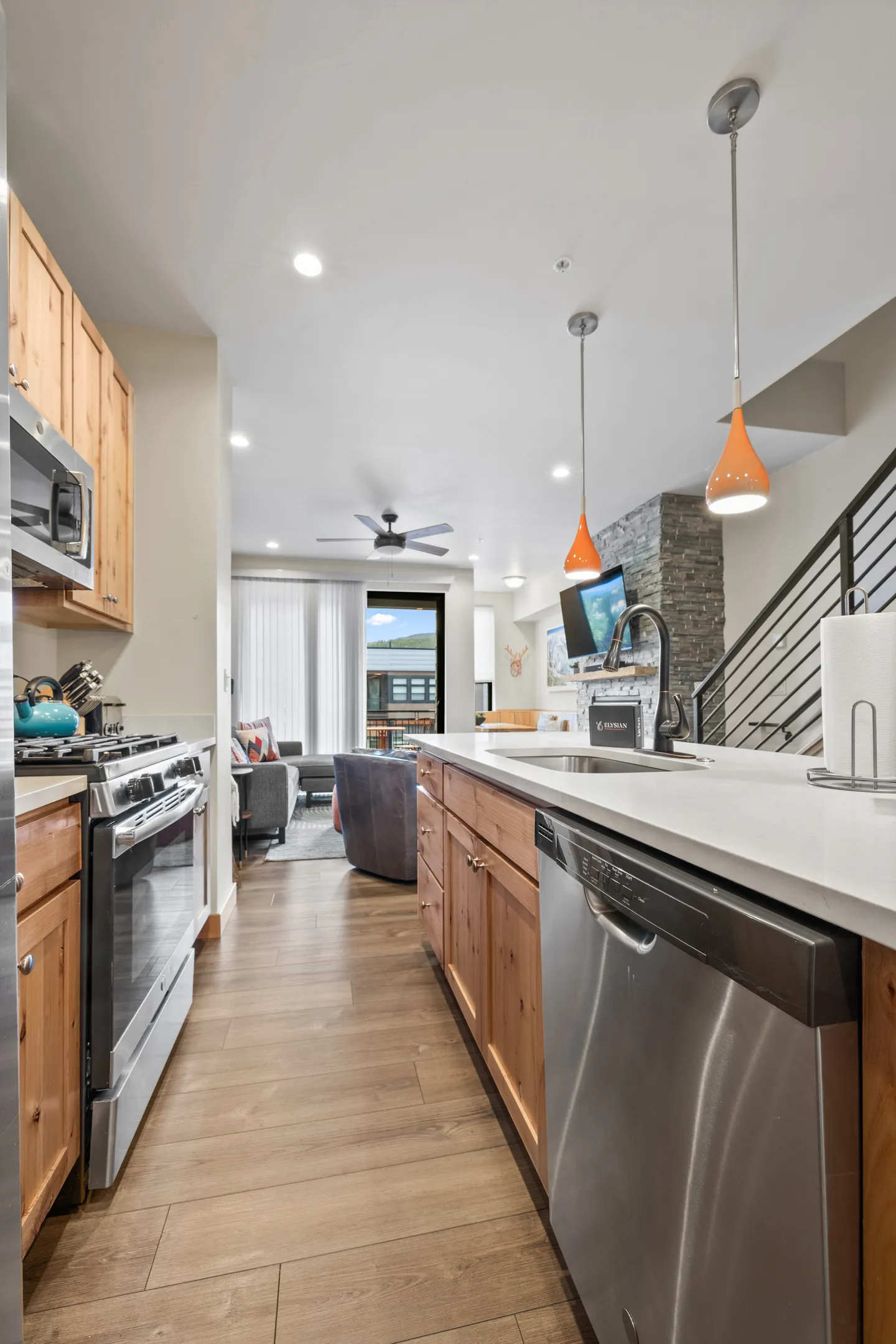 Open-concept kitchen with stainless steel appliances, light countertops, wood cabinets, and a view into the living room.