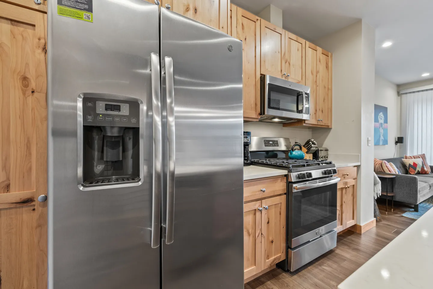 Close-up view of a kitchen featuring a stainless steel refrigerator with an exterior ice dispenser, light wood cabinetry, and a gas stove.