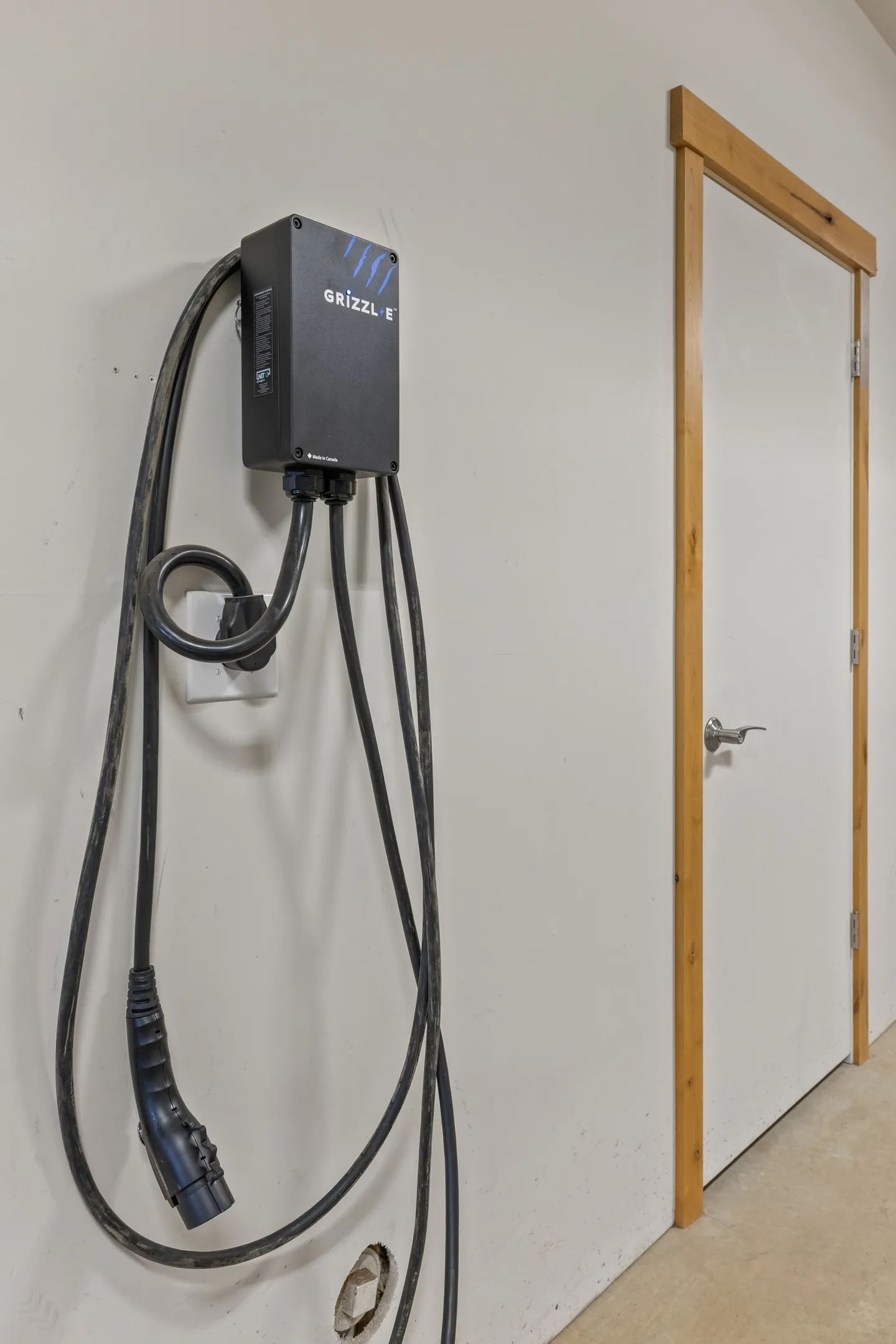 A wall-mounted Grizzl-E electric vehicle charging unit plugged into an outlet next to a door frame.