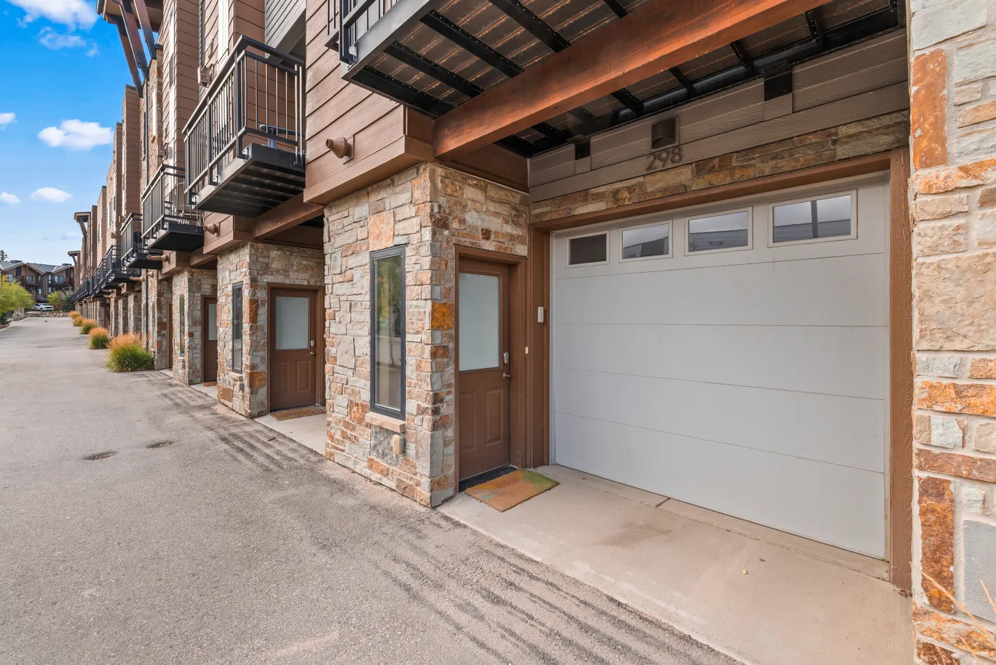 Exterior ground level of attached townhomes featuring stone pillars, brown siding, a single-car garage door, and entry doors.