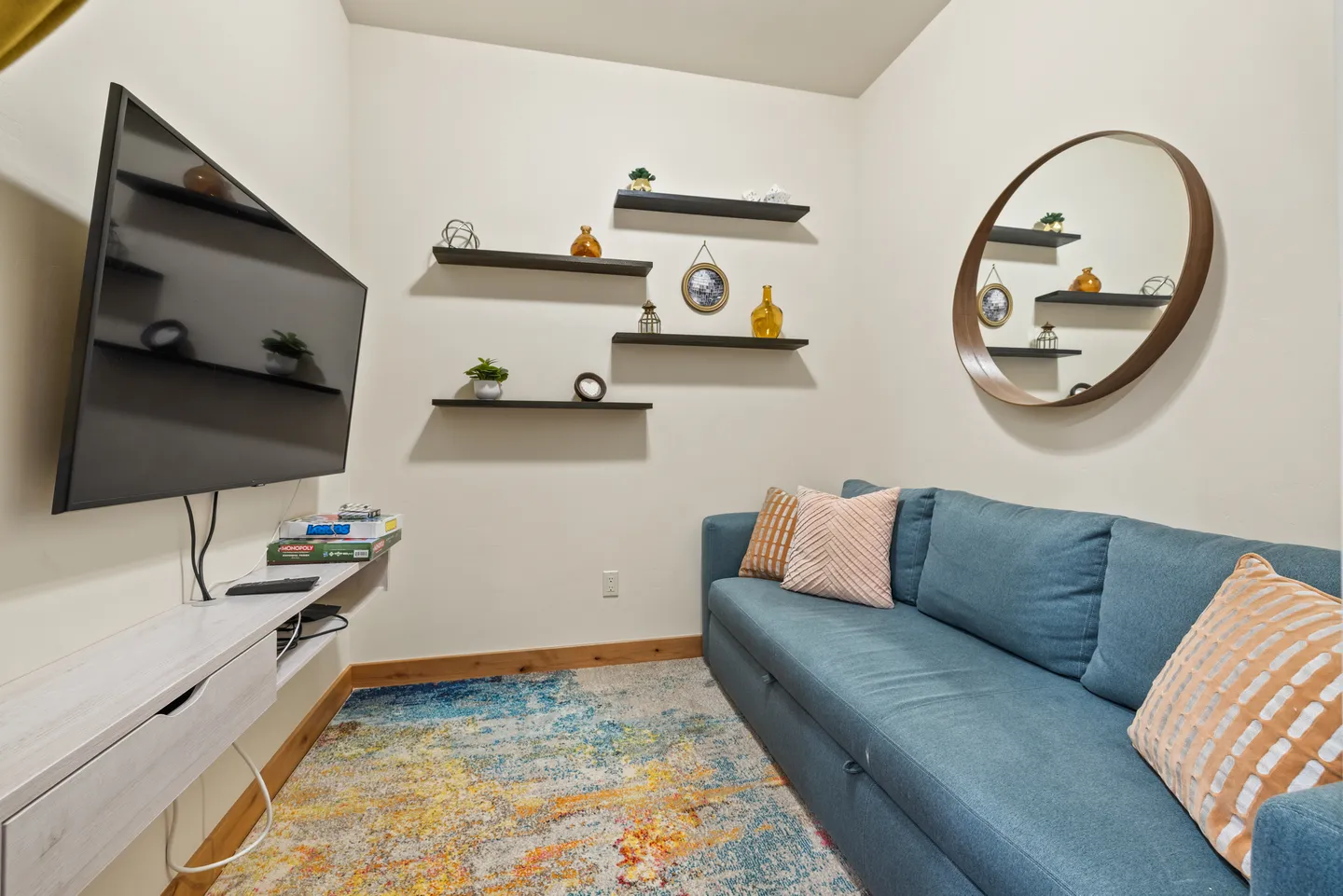 Cozy media nook featuring a blue sofa, colorful area rug, wall-mounted television, and floating display shelves.