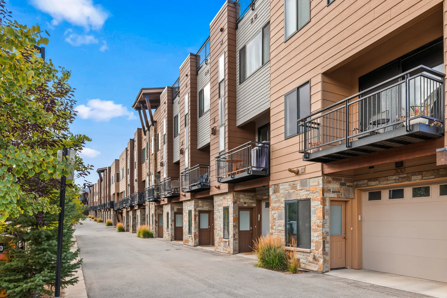Exterior view of a multi-story modern townhome complex with stone accents, wood siding, and metal balconies.