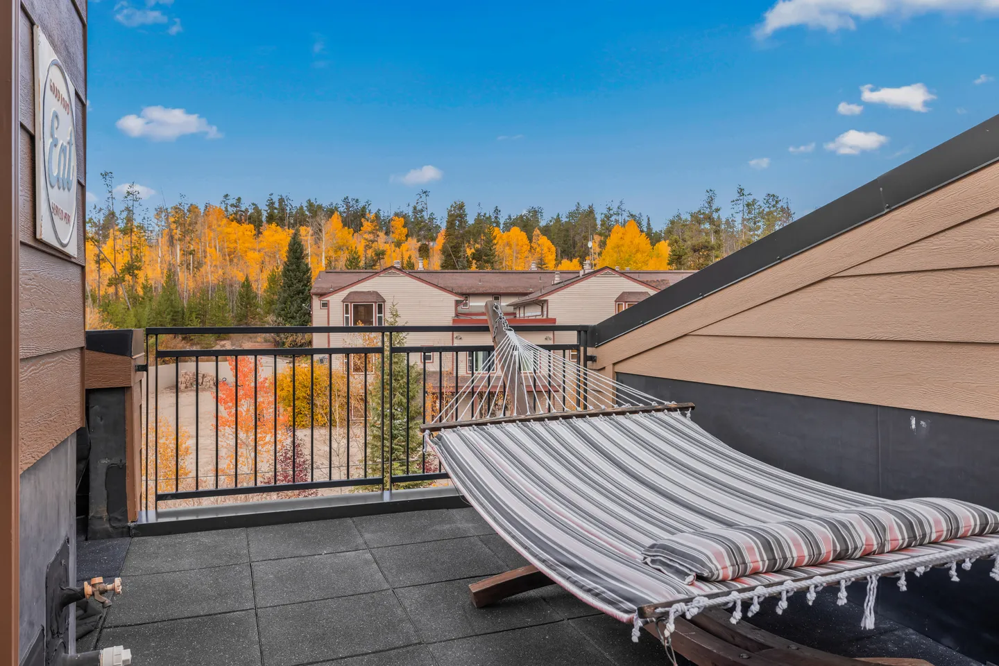 Outdoor balcony featuring a striped hammock on a wooden stand overlooking trees with vibrant autumn foliage.