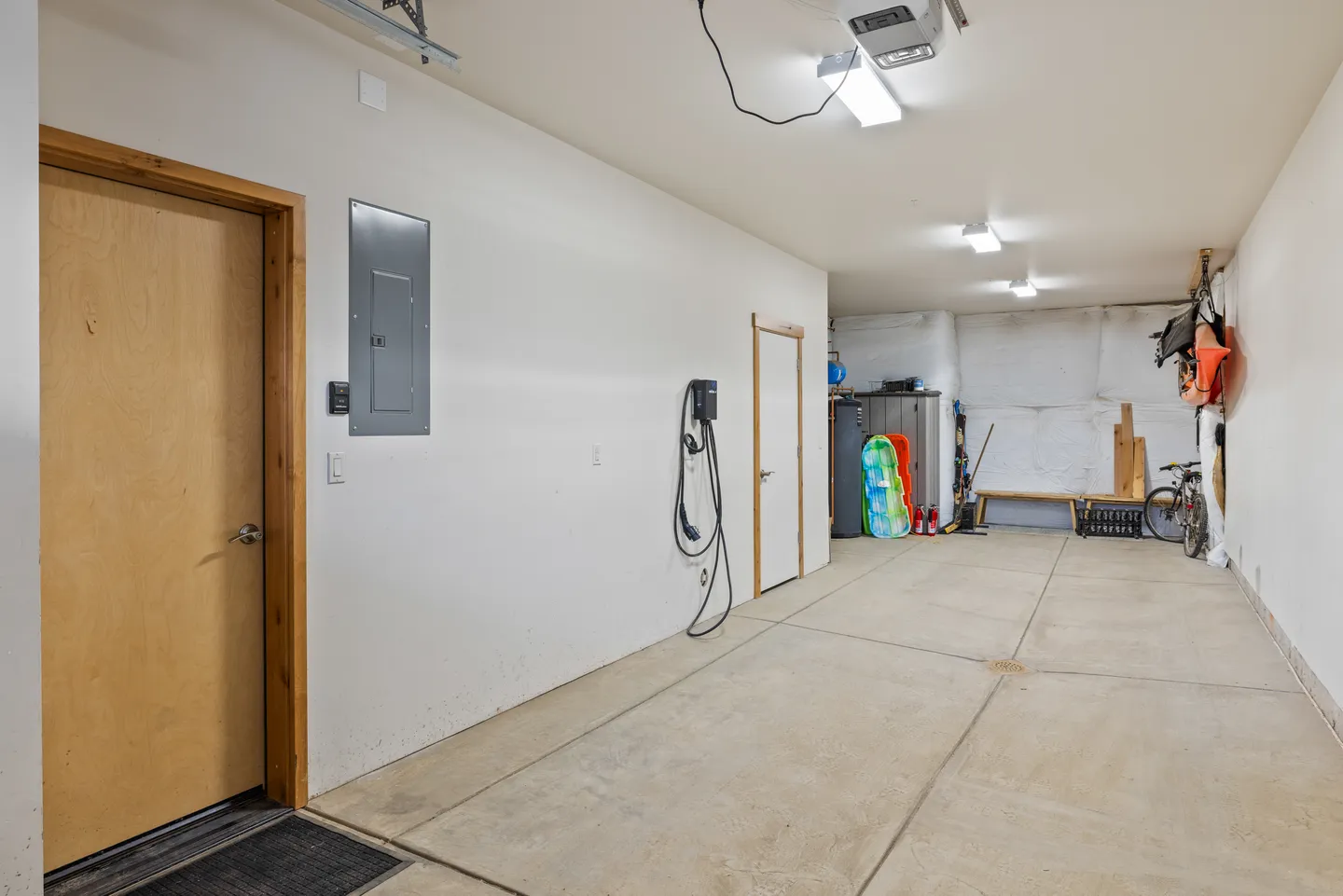 Spacious attached garage with concrete floor, white walls, electric vehicle charger, and interior access doors.