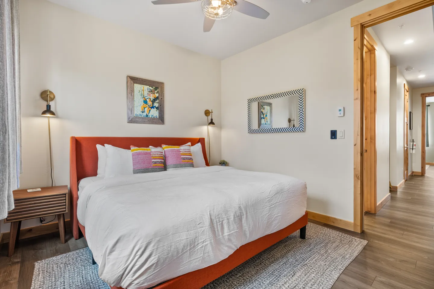 Bedroom with an orange upholstered bed frame, white bedding, accent pillows, wall sconces, and an open doorway leading to a hallway.