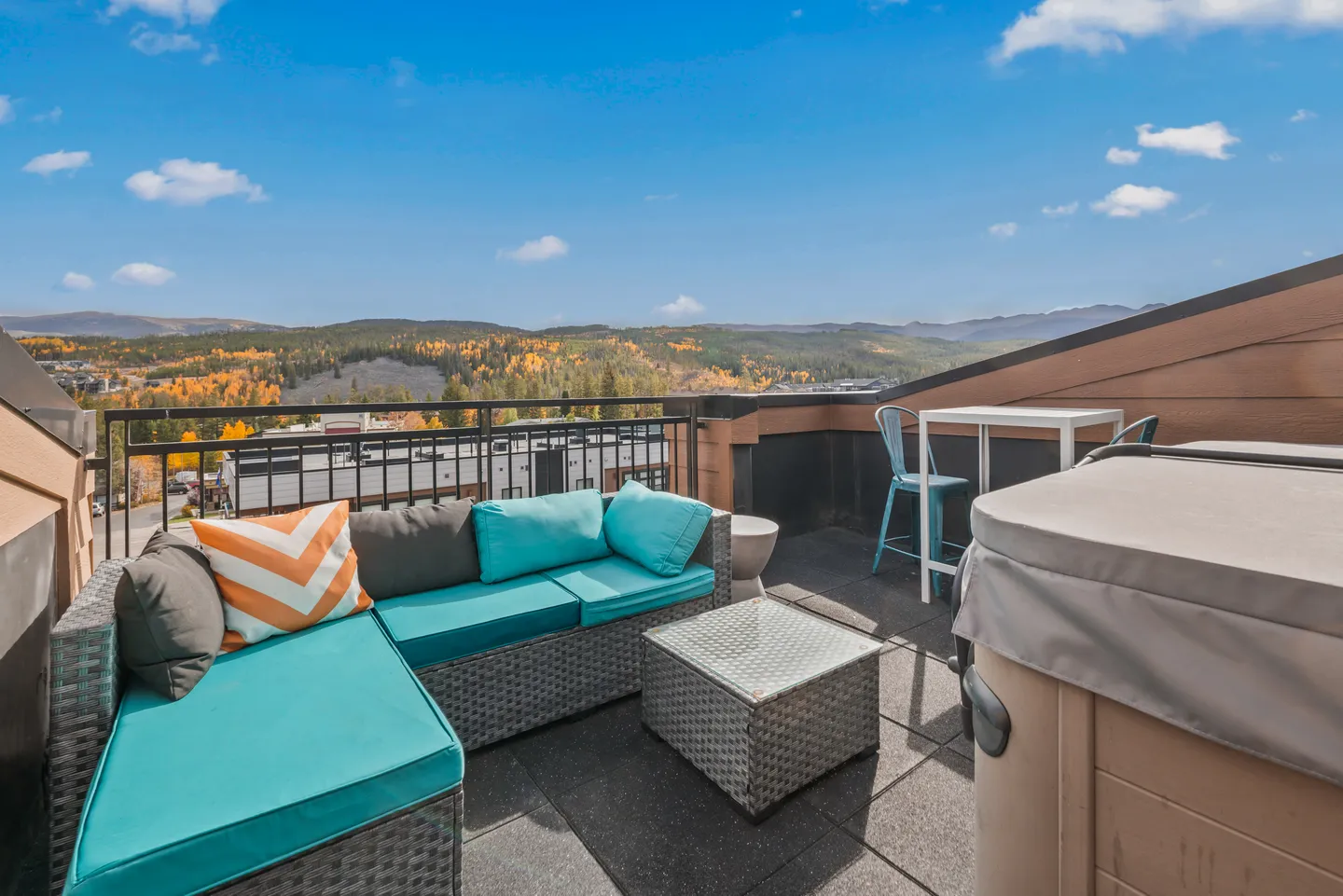 Rooftop patio with wicker sectional sofa, covered hot tub, and view of mountains and autumn trees.