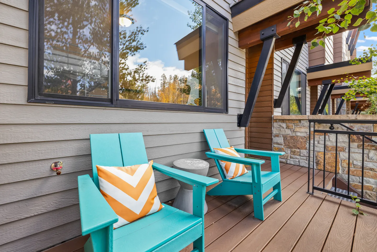 Two bright turquoise armchairs with orange and white chevron pillows on an outdoor covered deck.