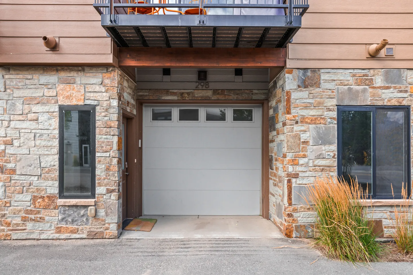 Exterior view of an attached single-car garage framed by stone veneer walls beneath an upper balcony.