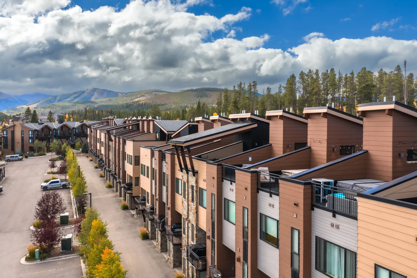 Elevated view of modern multi-story townhomes with wood and stone siding lining a street against a mountain backdrop.