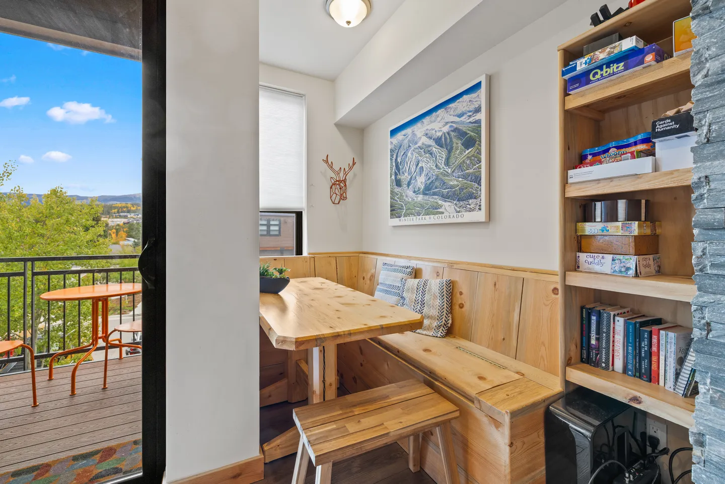 Dining nook with a wooden corner bench, table, and bench, next to a balcony and a built-in bookshelf.