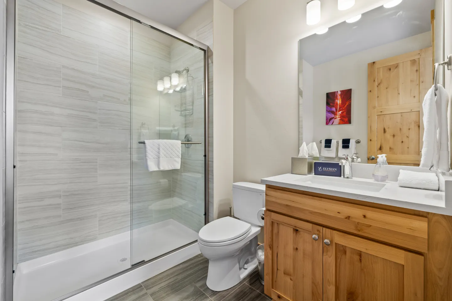 Bathroom with a glass-enclosed walk-in shower, toilet, and wood vanity with white countertop.