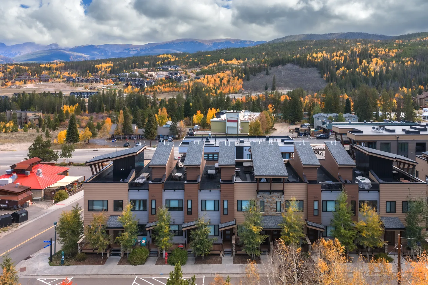 Aerial view of a multi-story townhome development surrounded by fall foliage with mountain ranges in the background.