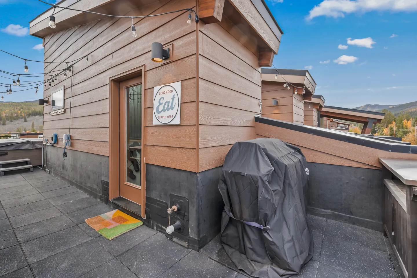 Rooftop patio with a covered barbecue grill, string lights overhead, and wood-look siding.