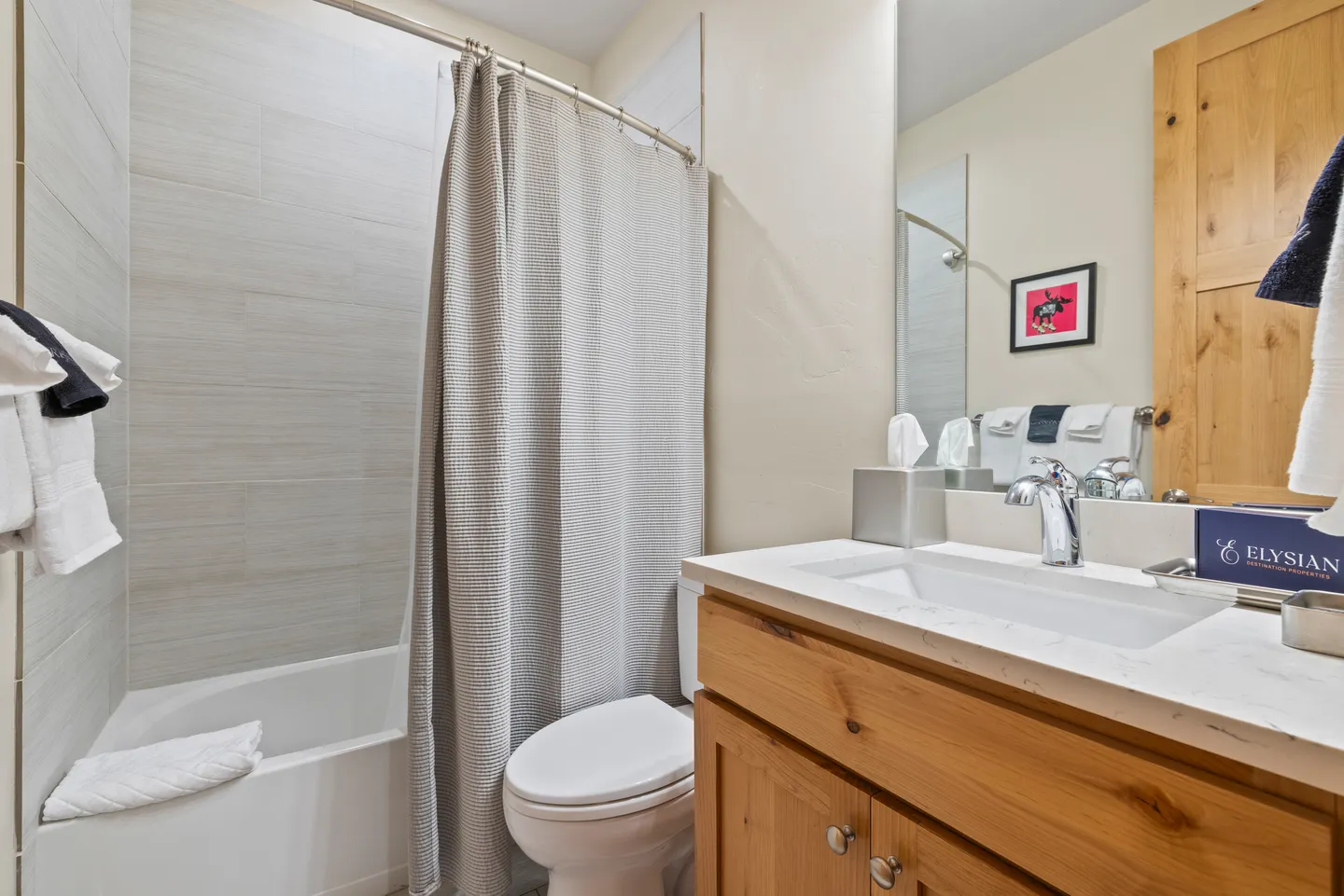 Bathroom with a wood vanity, white countertop, toilet, and bathtub with tiled walls and a curtain.