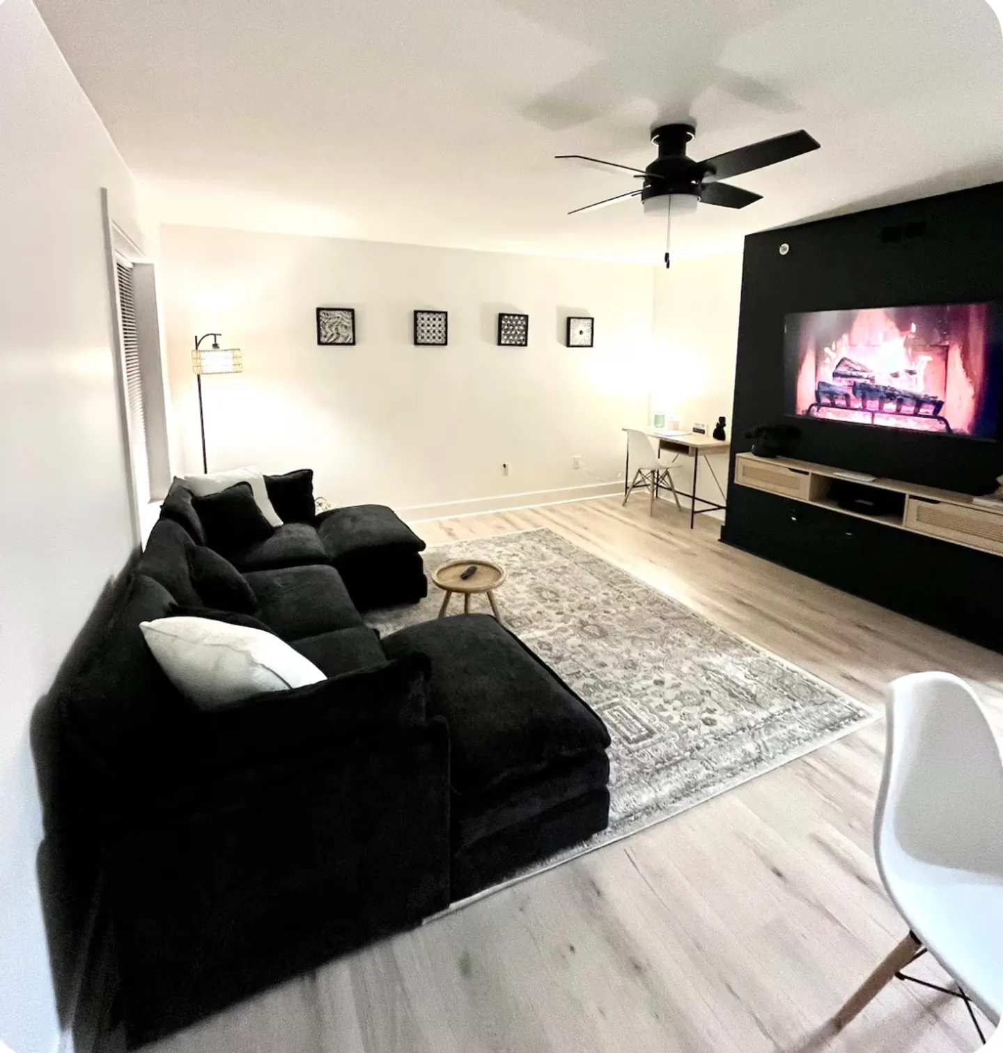 Living room with a large dark sectional sofa, area rug, wall-mounted television, and a small desk in the corner.