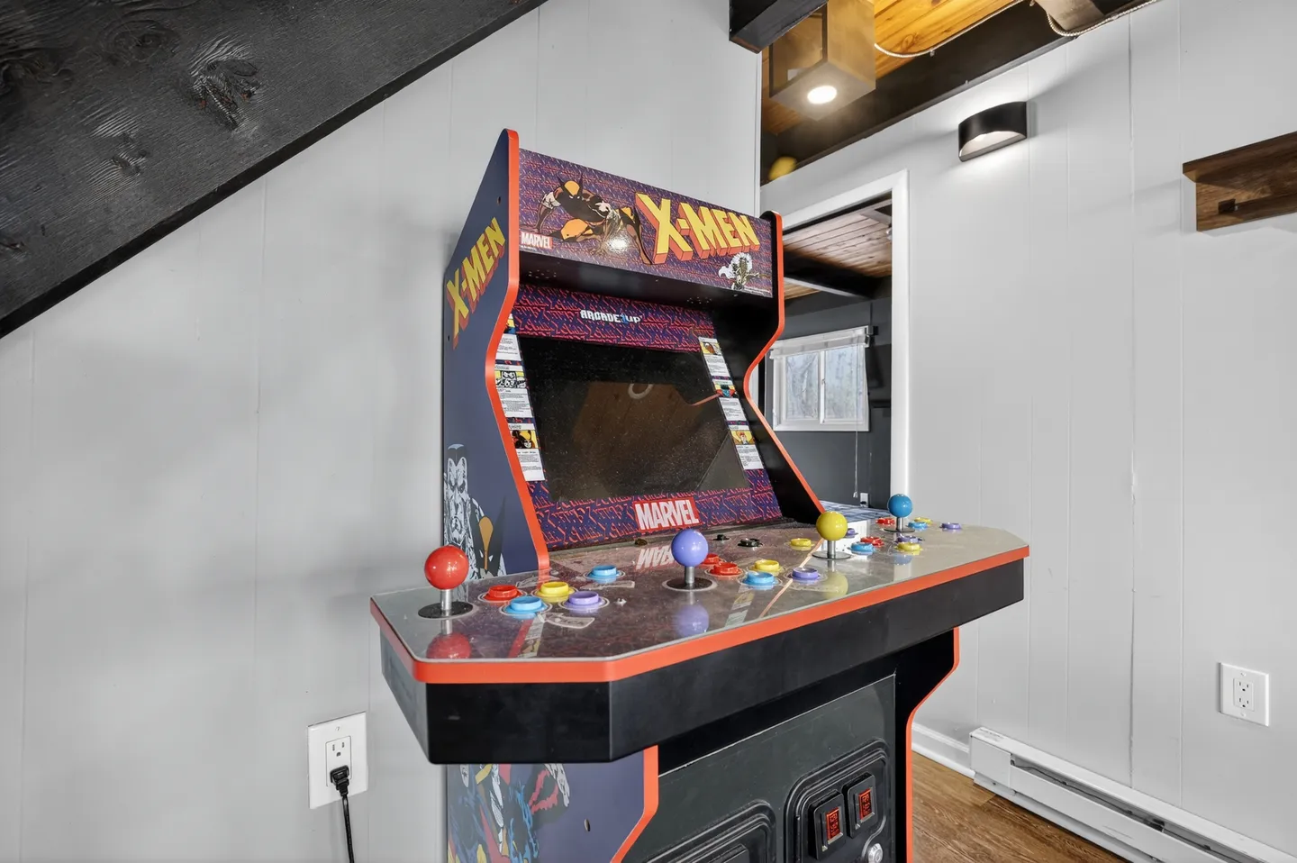 A Marvel X-Men arcade cabinet tucked under a staircase against paneled walls.