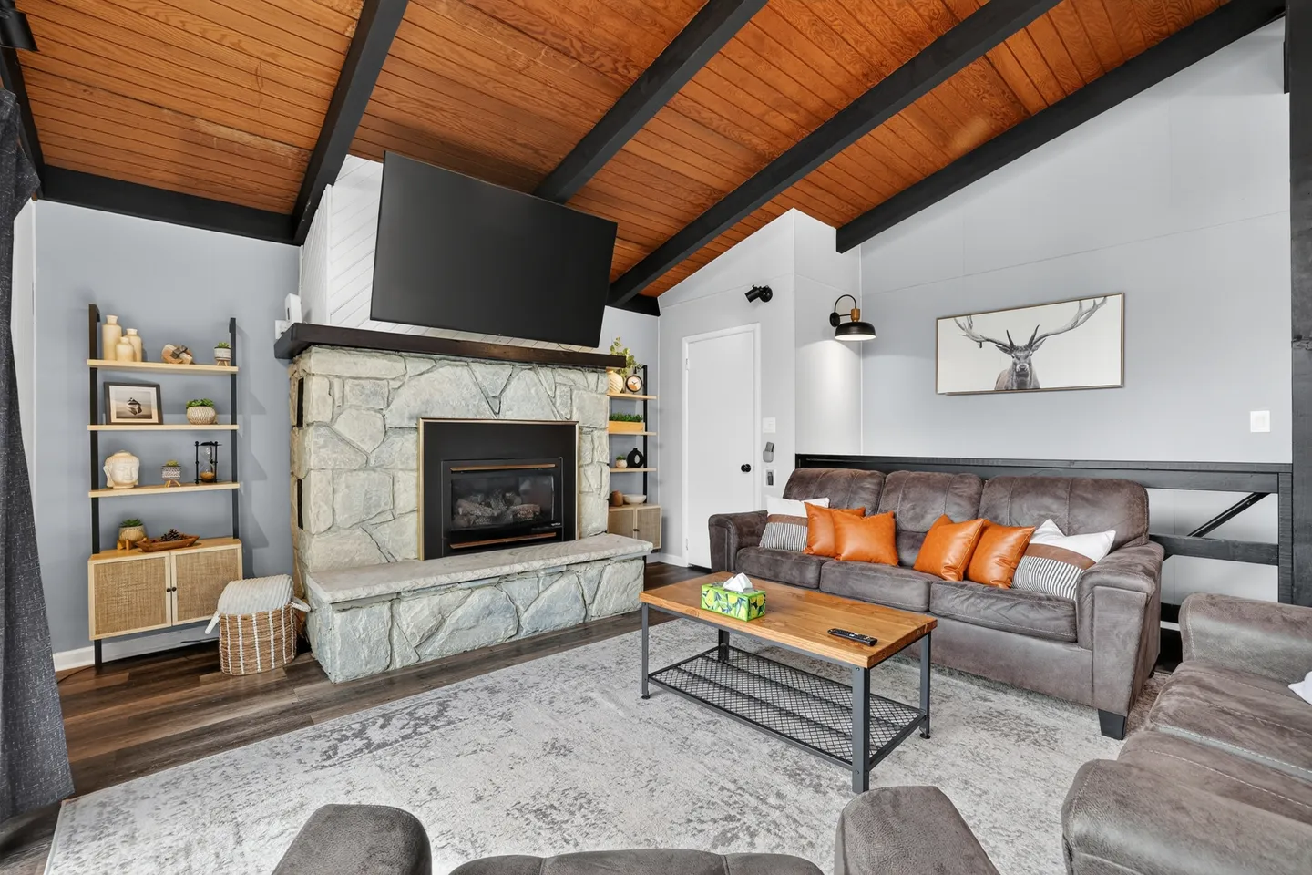 Living room with vaulted wood-paneled ceiling, stone fireplace with mounted television, and leather seating.