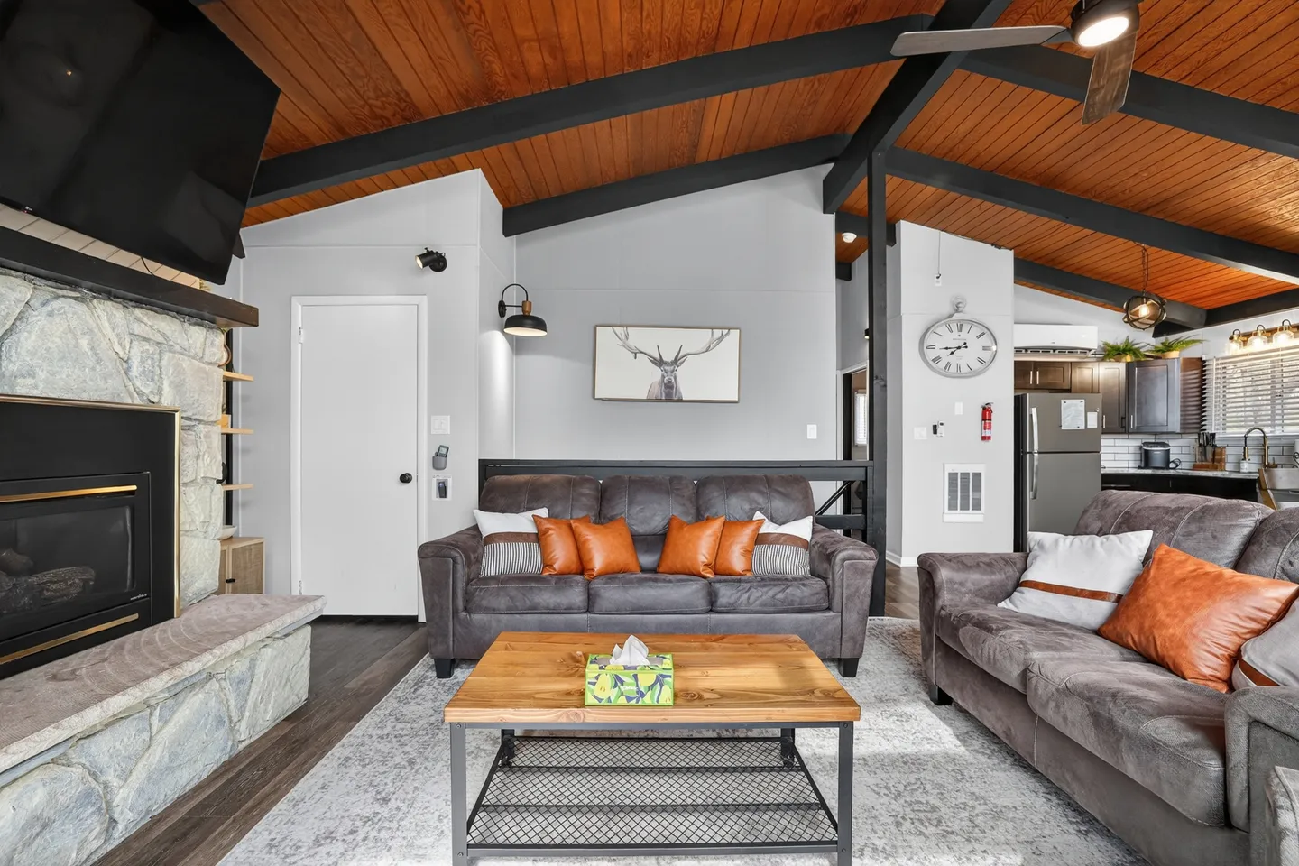 Living room featuring vaulted wood-paneled ceilings with dark beams, a stone fireplace, and comfortable sofas arranged around a wood and metal coffee table.