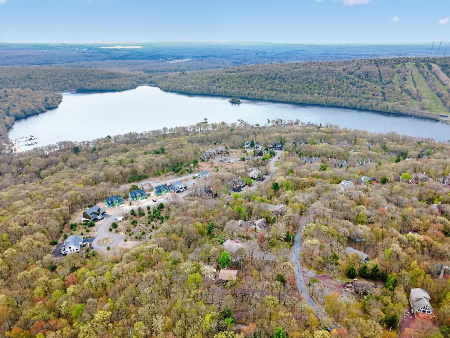 Aerial view of a wooded residential community bordering a large lake with rolling forested hills in the background.