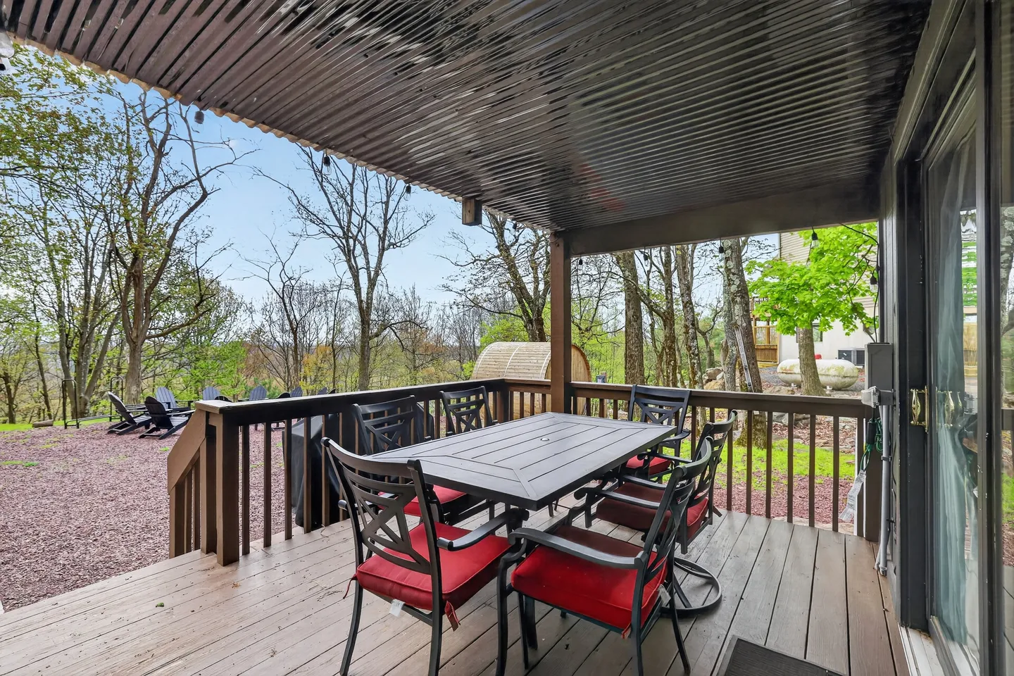 A covered outdoor deck with a dining table and chairs, overlooking a wooded yard.