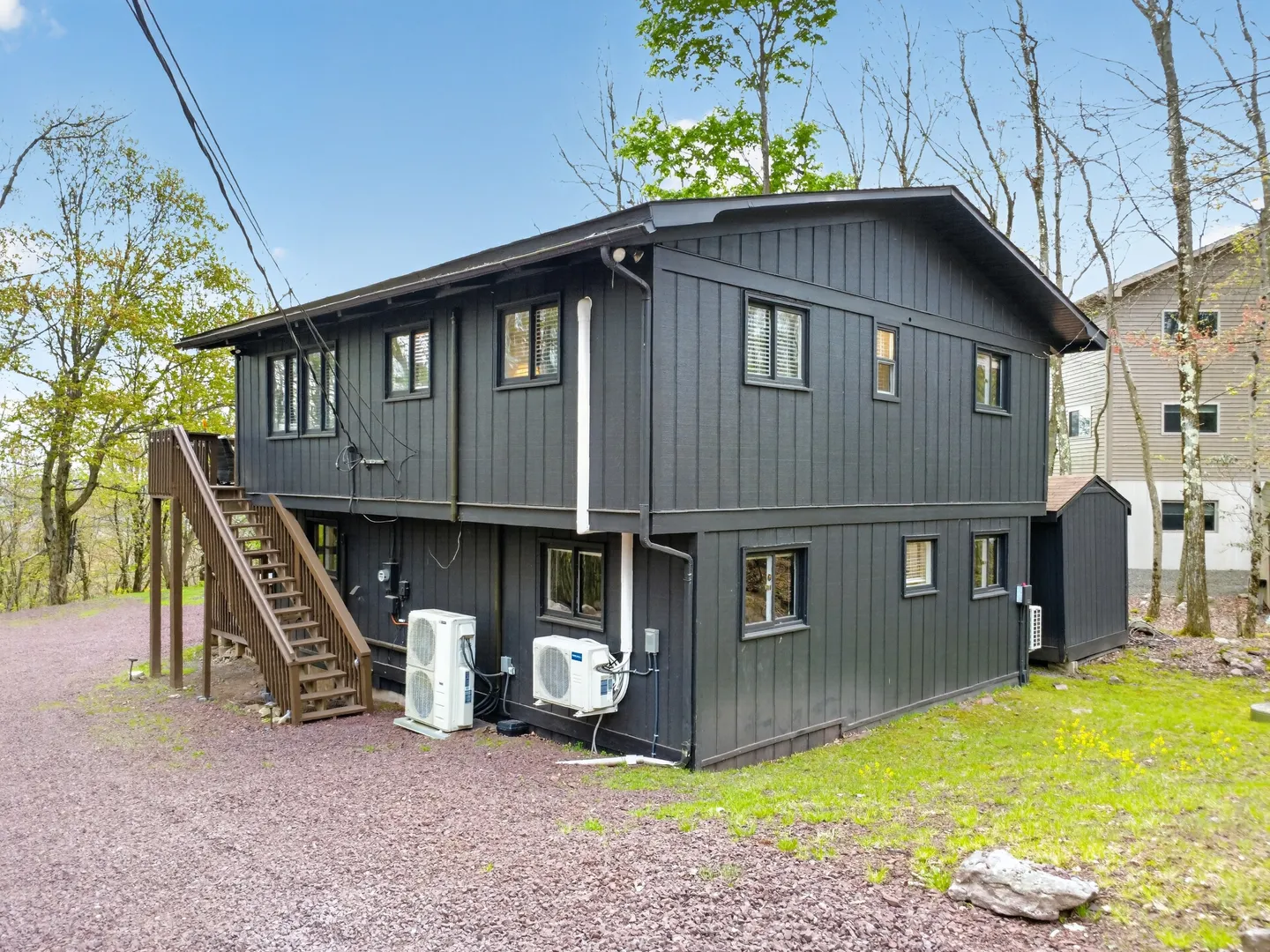 Exterior rear and side view of a two-story dark charcoal gray house with outdoor wooden stairs and mini-split units.