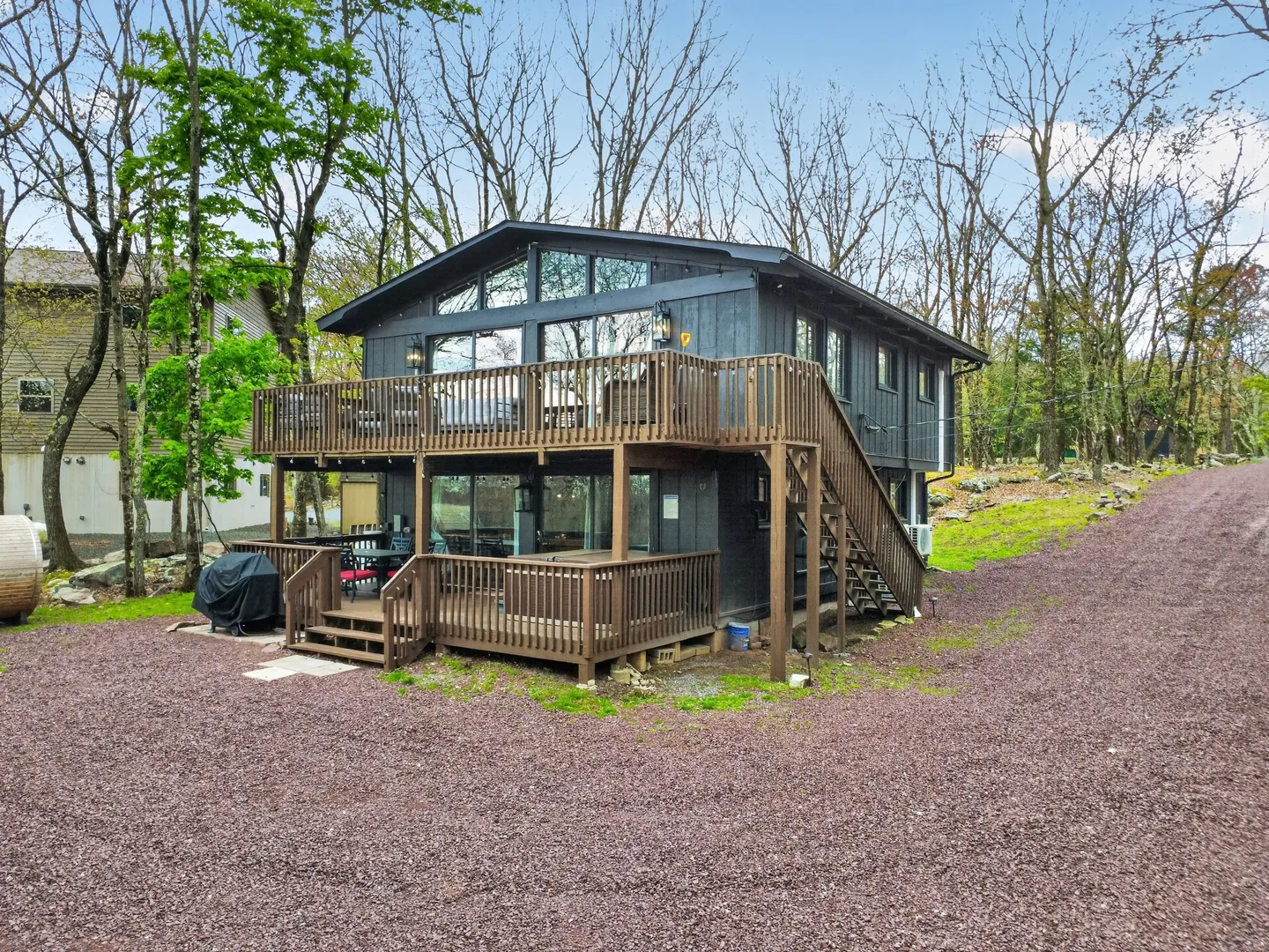Exterior rear view of a two-story dark wood house featuring upper and lower wooden decks set among tall trees.