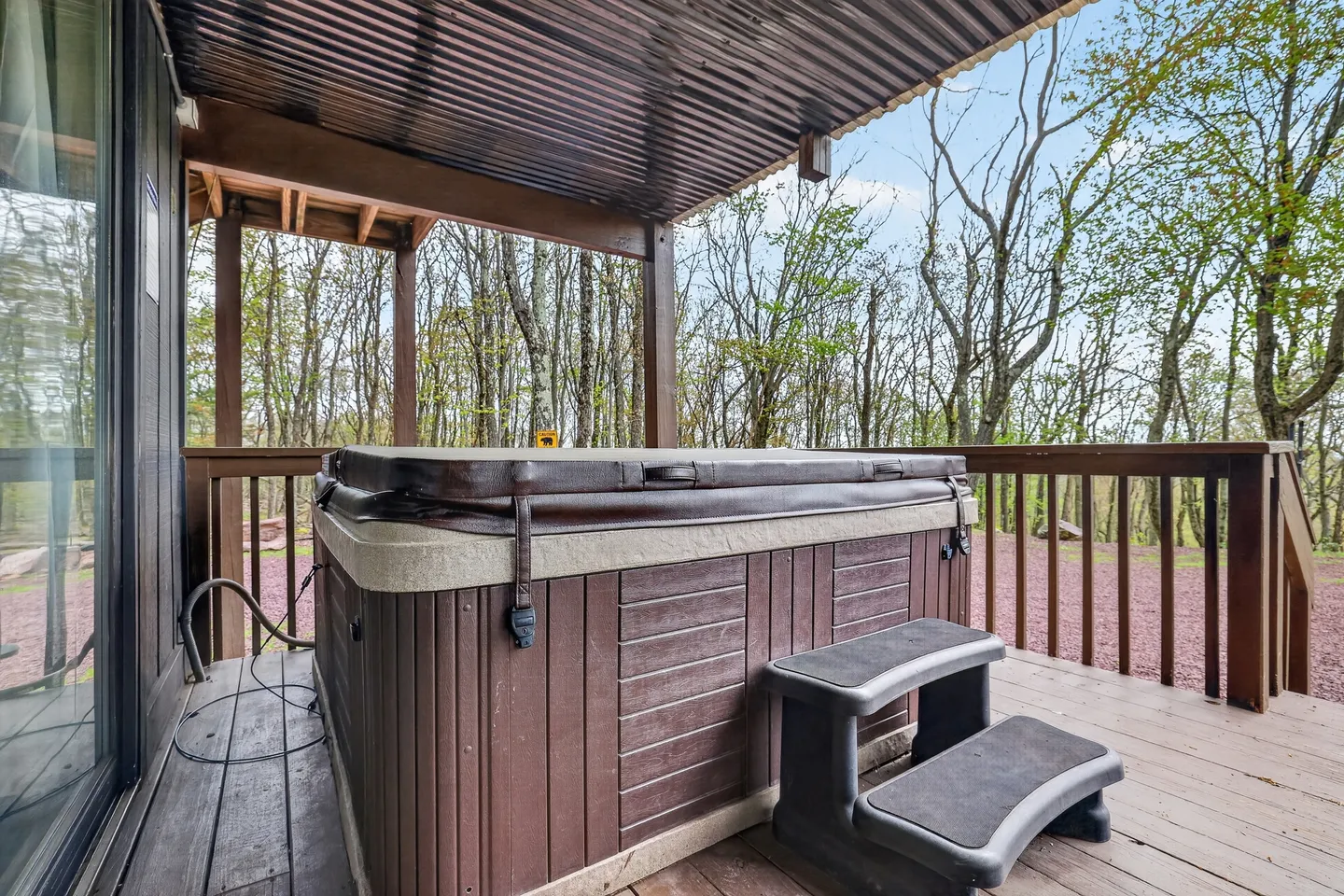 A covered hot tub with steps on an outdoor wooden deck surrounded by trees.