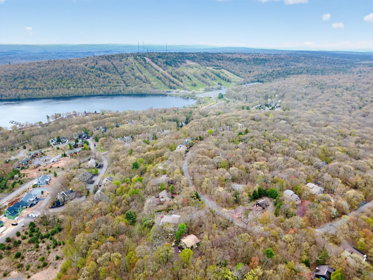 Aerial view of a wooded residential community bordering a lake with a ski mountain in the background.