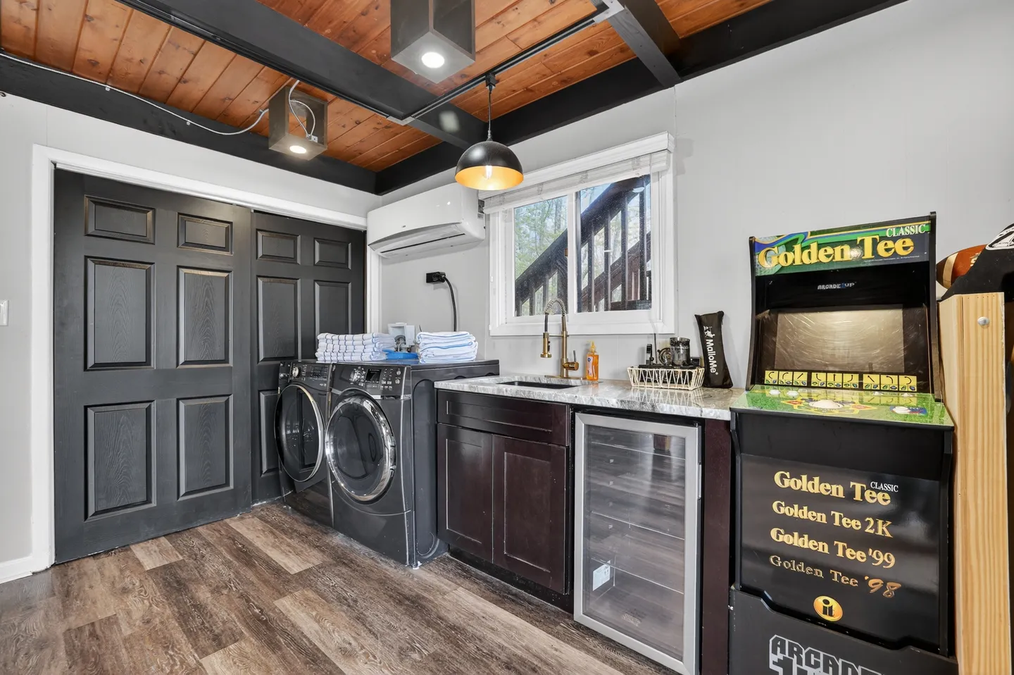 A utility and entertainment area with front-loading washer and dryer, small sink, mini beverage cooler, and arcade game cabinet.