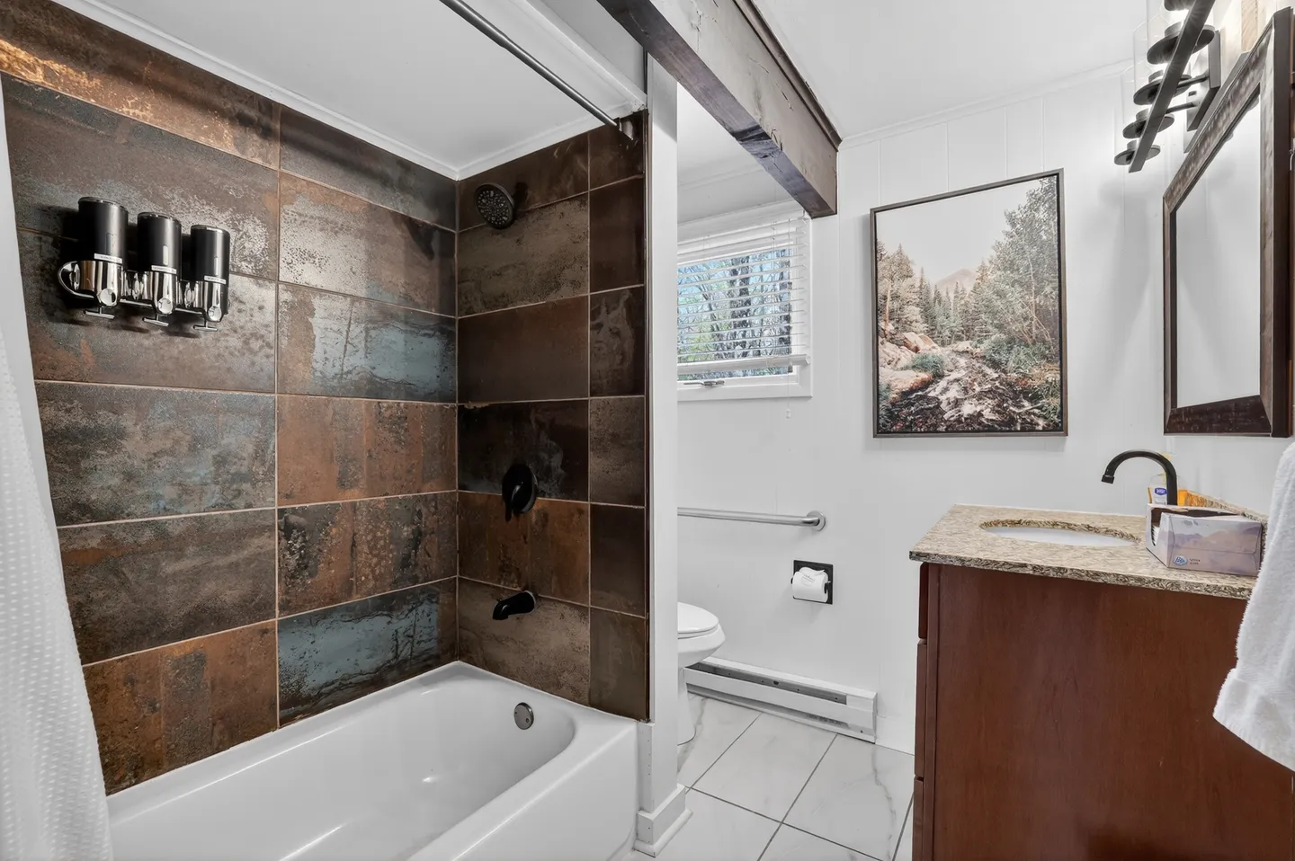 Bathroom showing a bathtub with shower surrounded by rust-colored metallic tiles, a wooden vanity with a black faucet, and a toilet in the background.