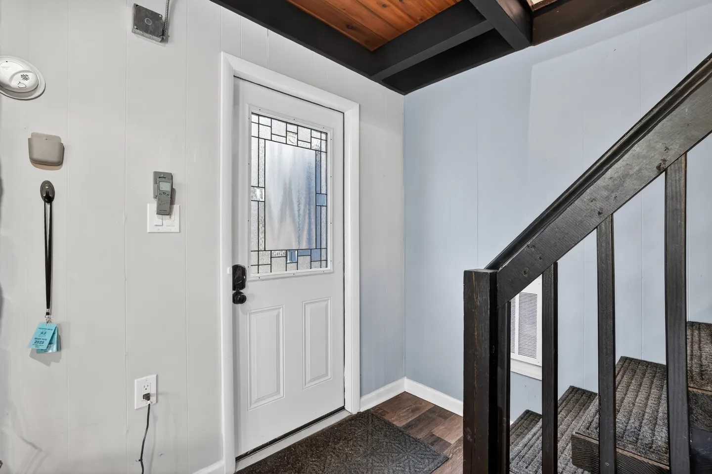 Front entry door with frosted decorative glass insert next to an interior dark wood staircase.