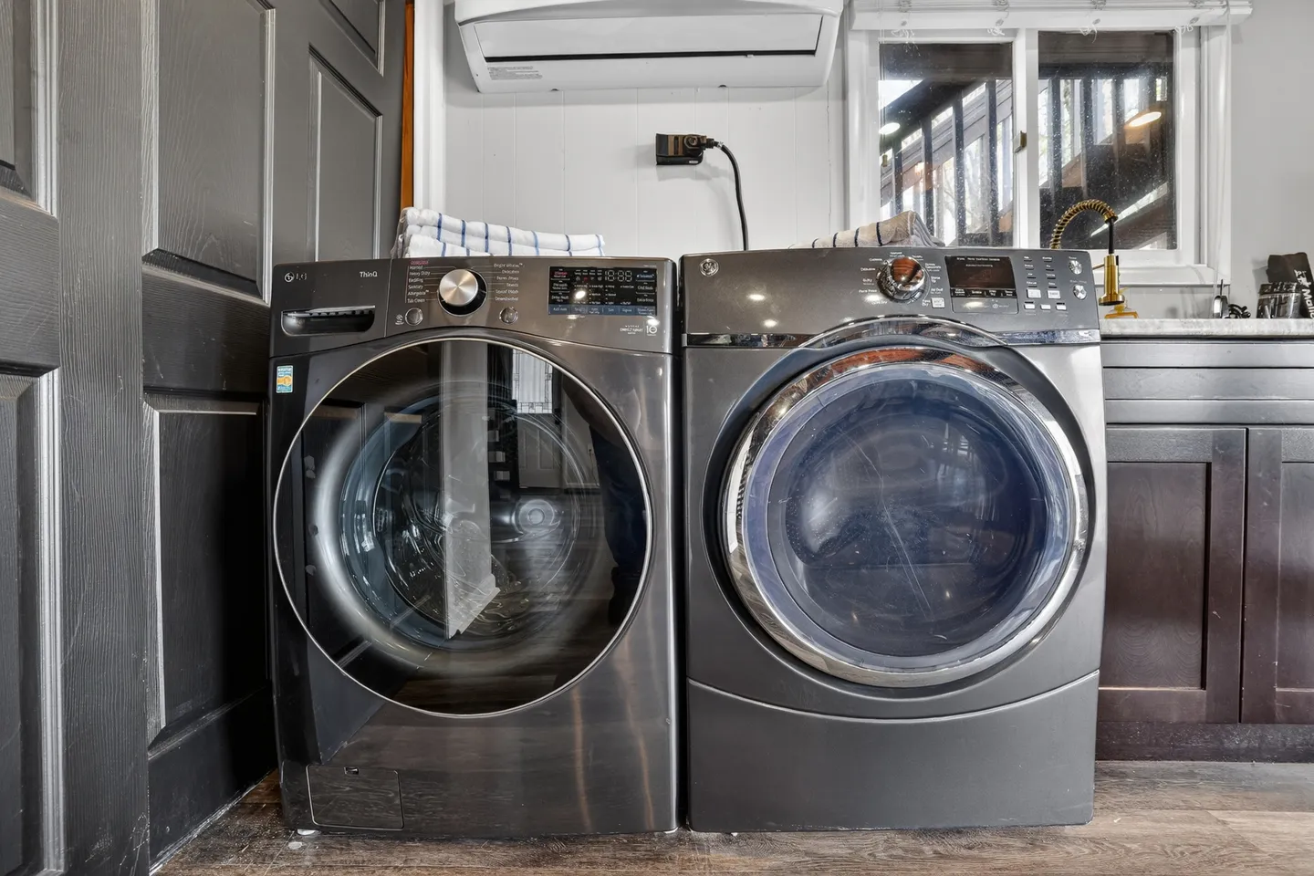 Front-loading washer and dryer set side by side indoors beneath a mini-split air conditioner.
