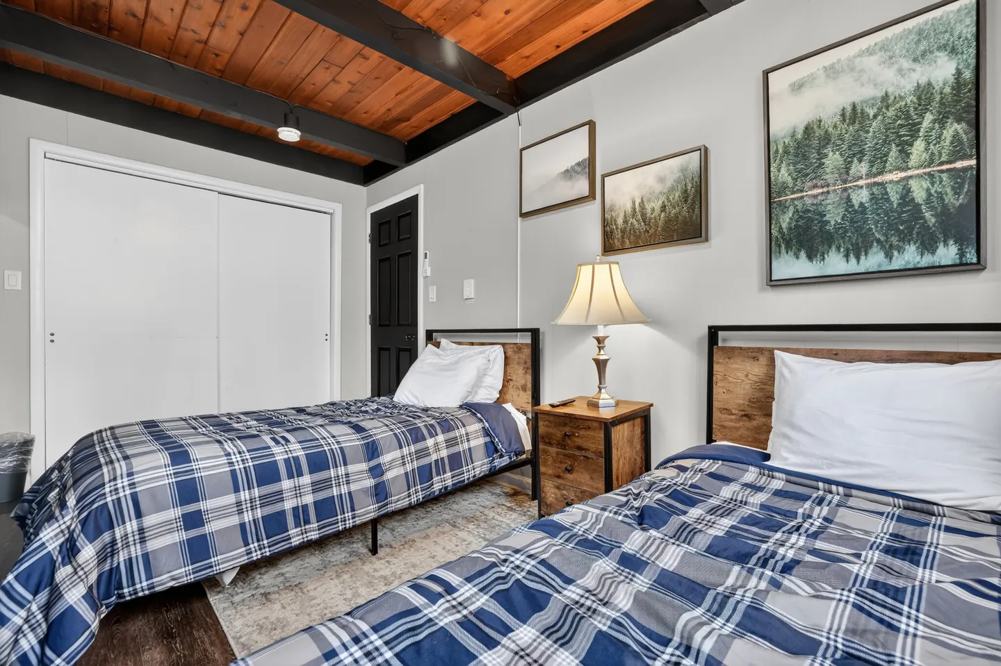 Bedroom featuring two single beds with blue plaid bedding, a wood-paneled ceiling with dark beams, and framed landscape prints on the wall.
