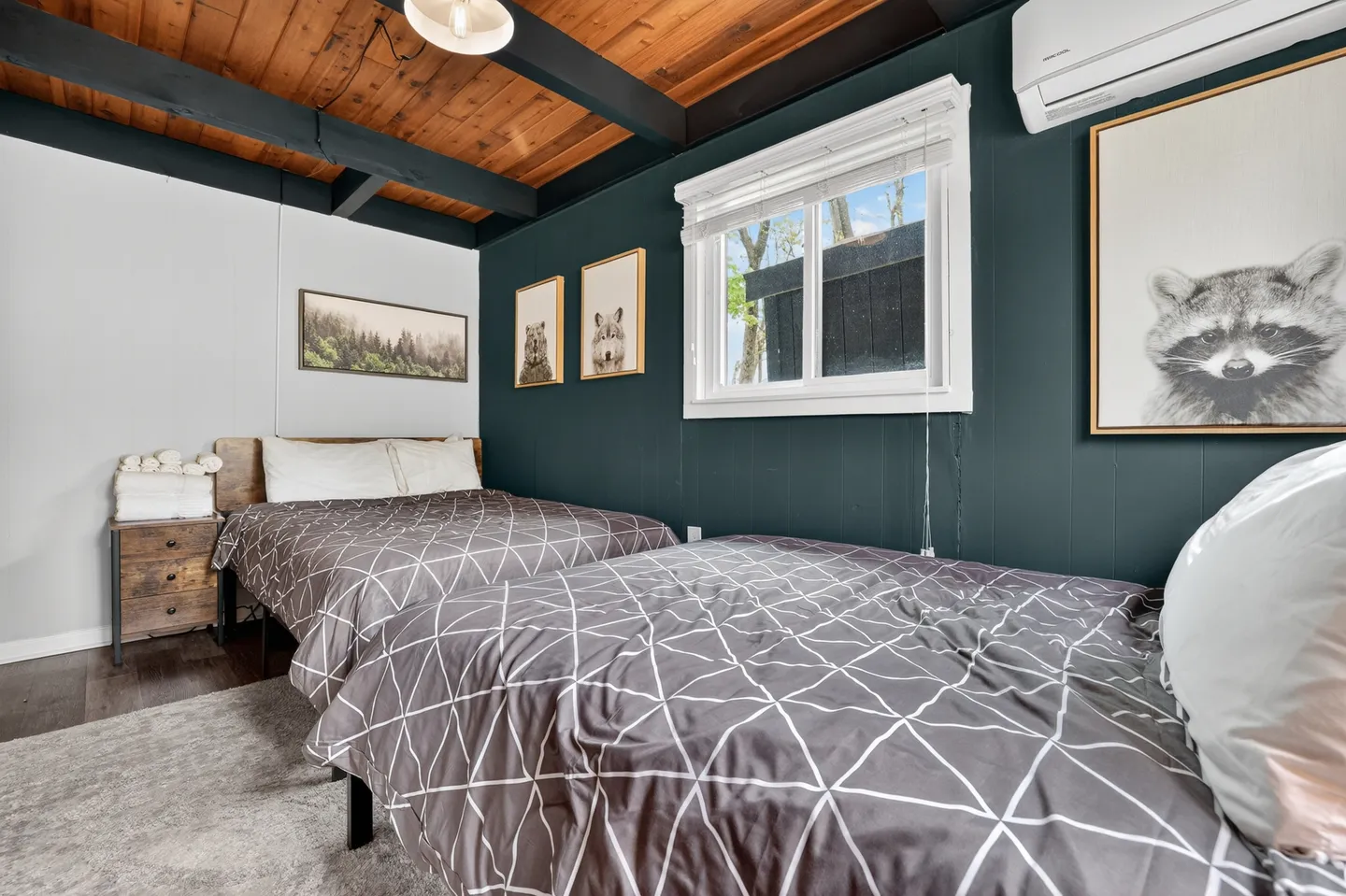 Bedroom with two beds, dark teal accent wall, wood-plank ceiling with dark beams, and framed animal artwork.