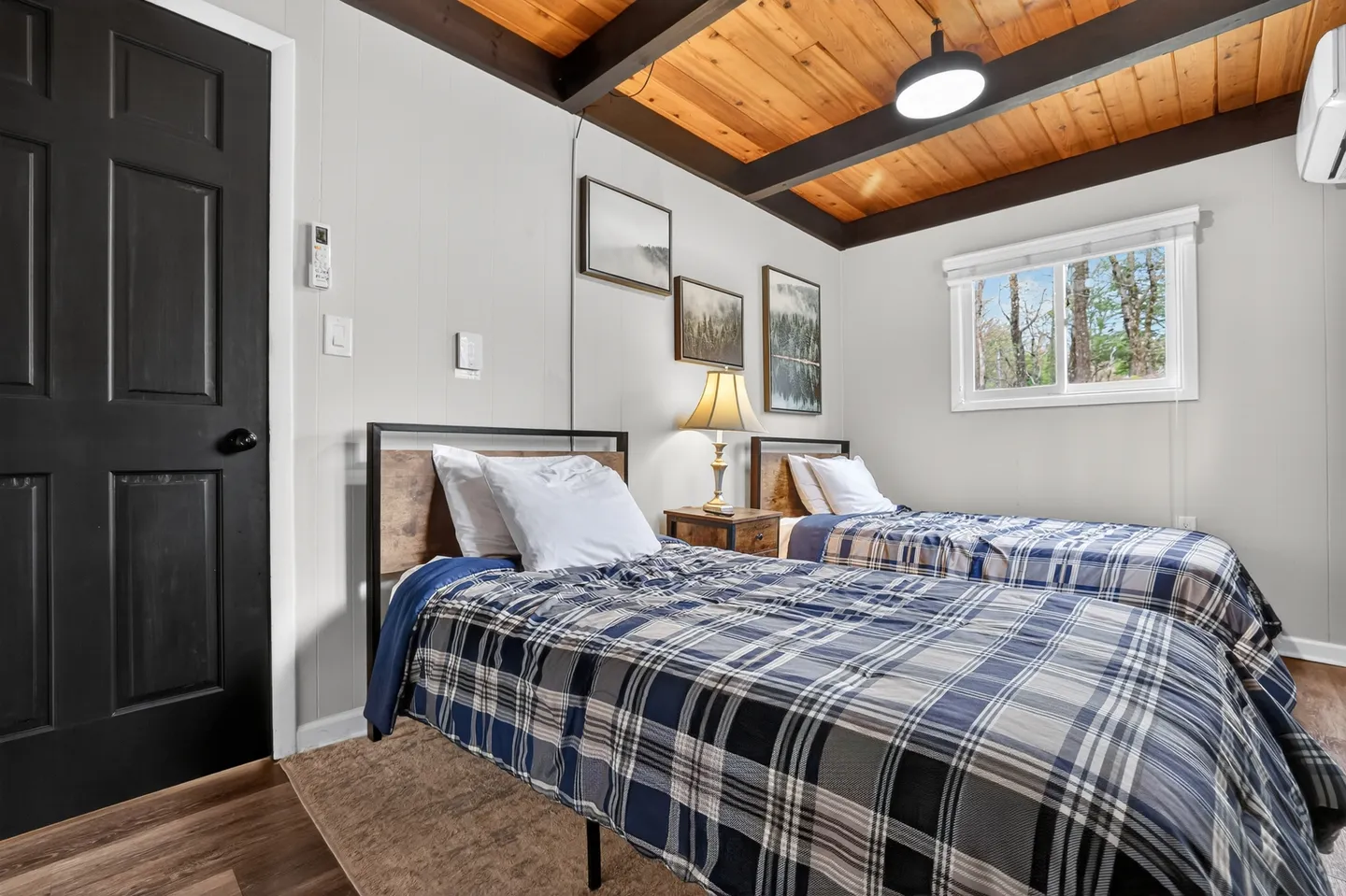 Bedroom with two twin beds dressed in blue plaid bedding, a wood-plank ceiling with dark beams, and a black door.