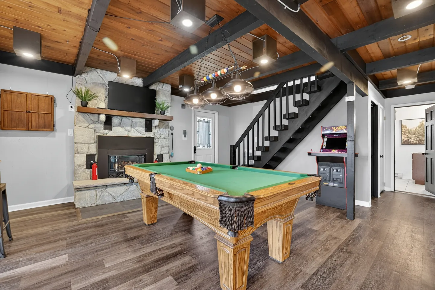 Game room featuring a wooden pool table, a stone fireplace with a television mounted above, and an open staircase.