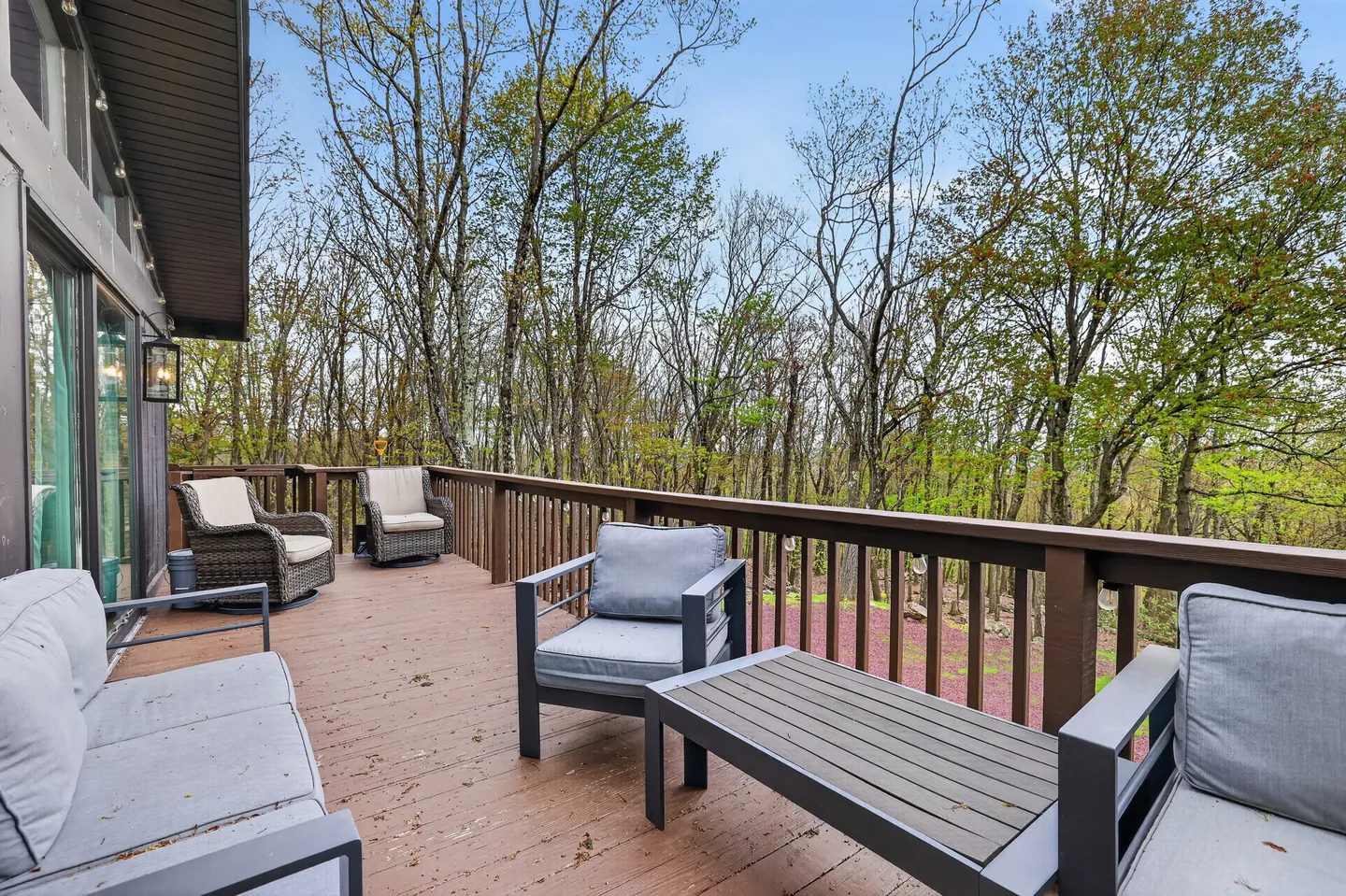 Outdoor wooden deck with patio furniture surrounded by trees under a blue sky.