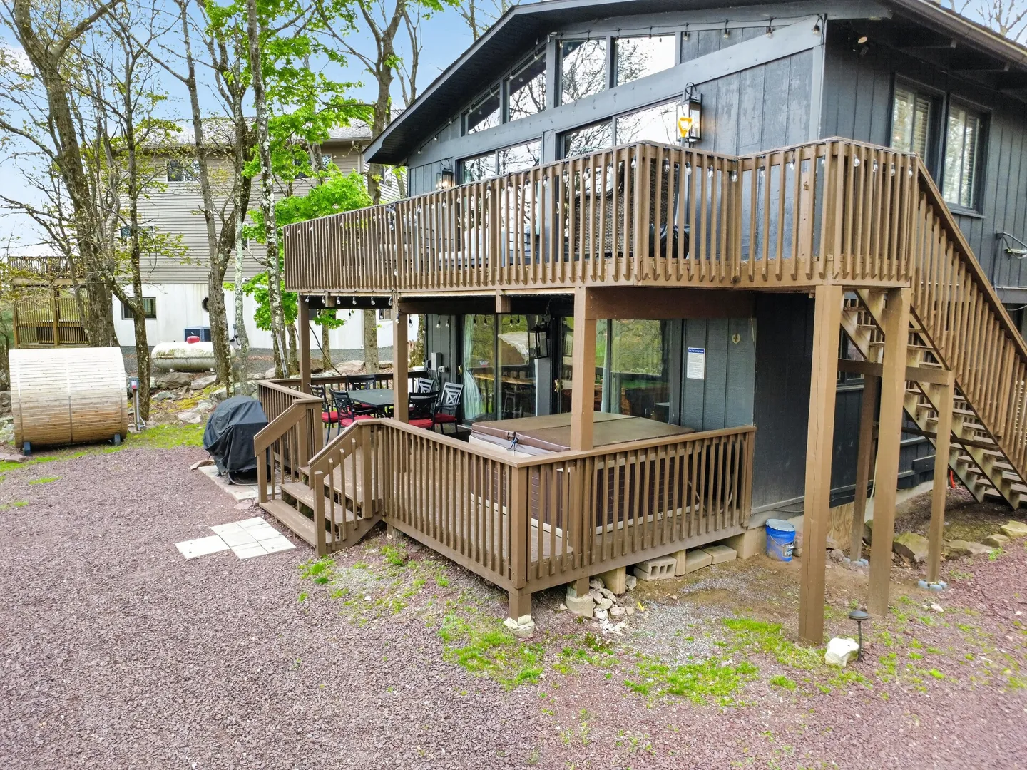 Exterior multi-level brown wooden deck attached to a dark siding home, featuring a hot tub on the lower deck and a covered patio area.