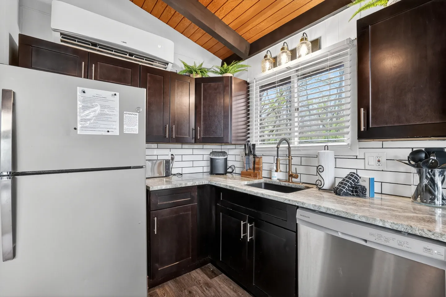 Kitchen corner featuring dark wood cabinets, light countertops, a white subway tile backsplash, a sink beneath a window, and stainless-look appliances.