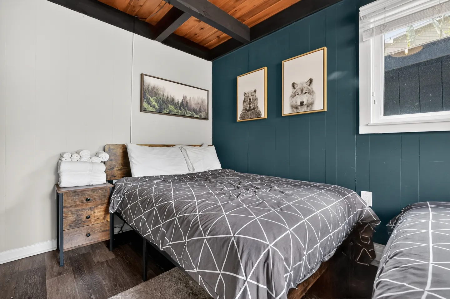 Bedroom featuring a bed with a geometric patterned comforter, a wood-panel accent wall in deep teal, and framed wildlife prints.