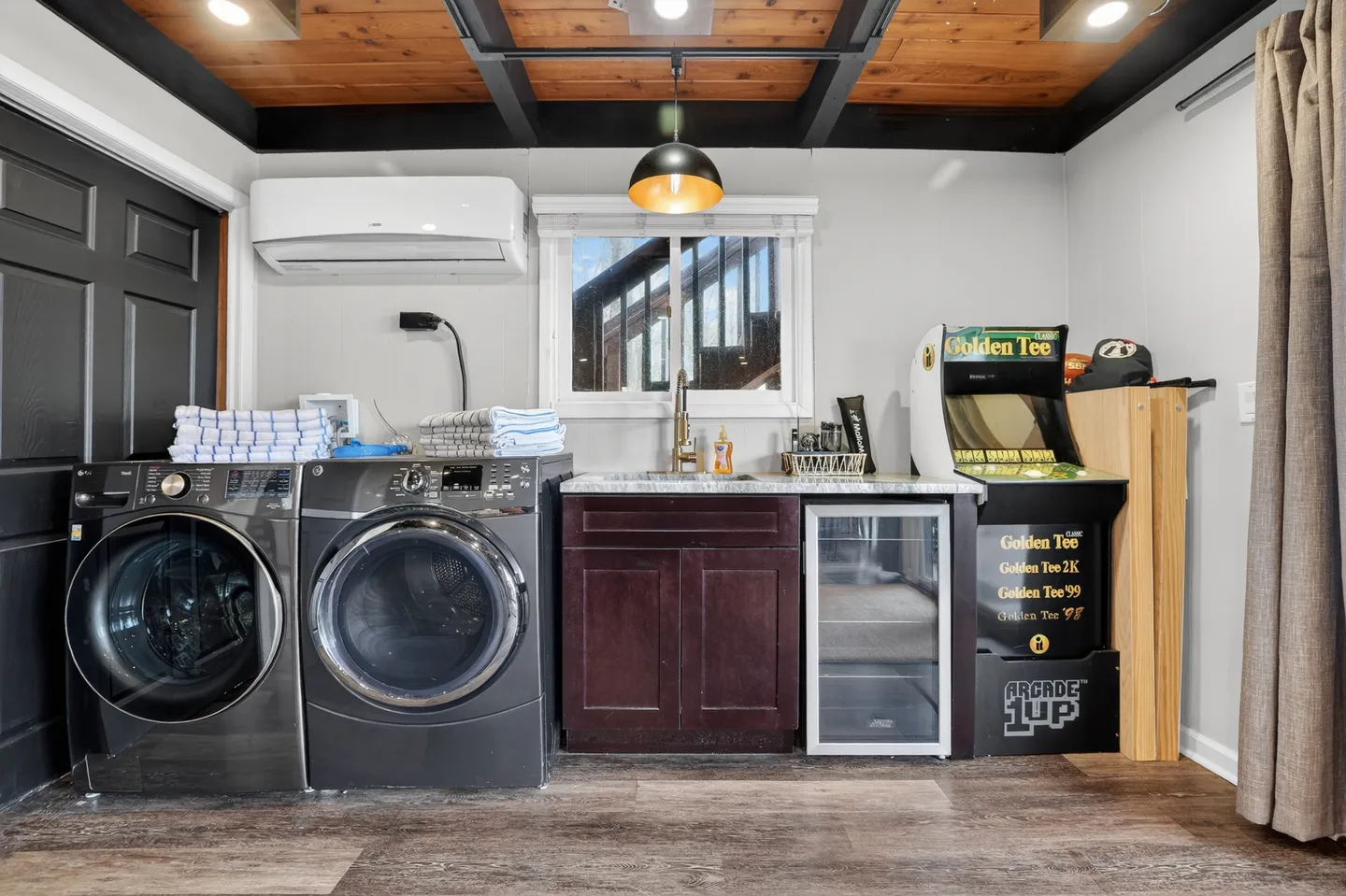 Laundry and entertainment corner with a washer, dryer, wet bar sink, mini fridge, and arcade game machine.