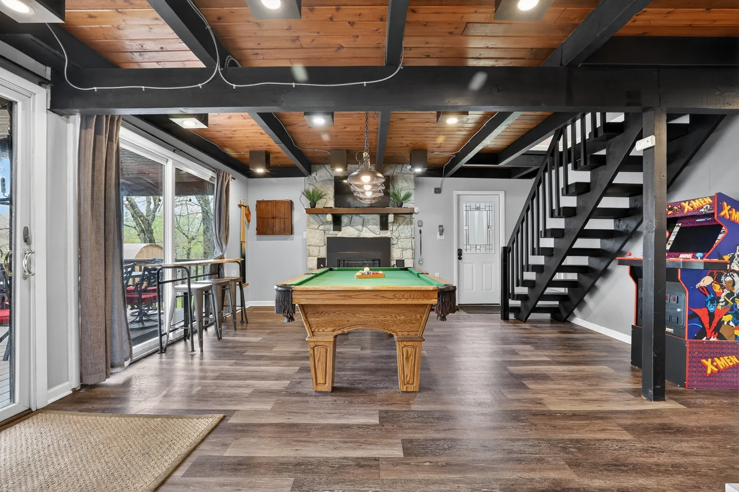 Game room featuring a wooden pool table, an arcade cabinet, a stone fireplace, and stairs under exposed ceiling beams.